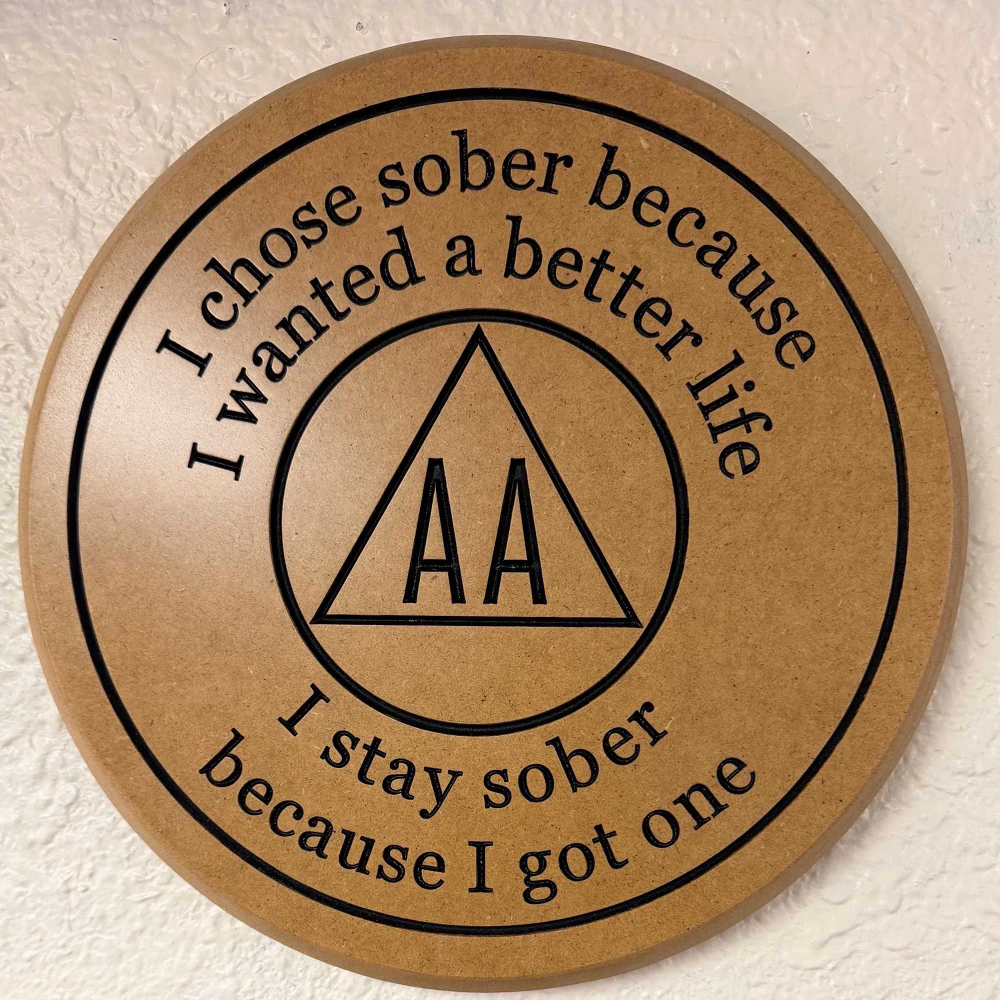 Close-up of a circular tan-colored sign with black text that reads, "I chose sobriety because I wanted a better life. I stay sober because I like it." The sign is mounted on a textured white wall.