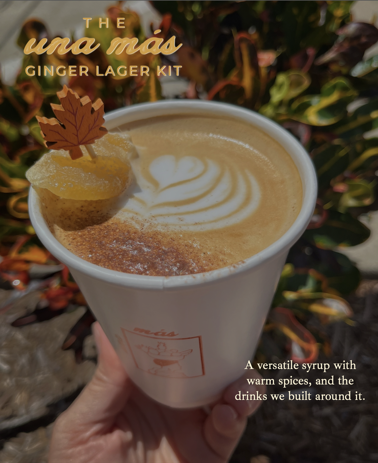 A cup of ginger latte with latte art, garnished with lemon and a decorative leaf, held outdoors with fall foliage in the background.