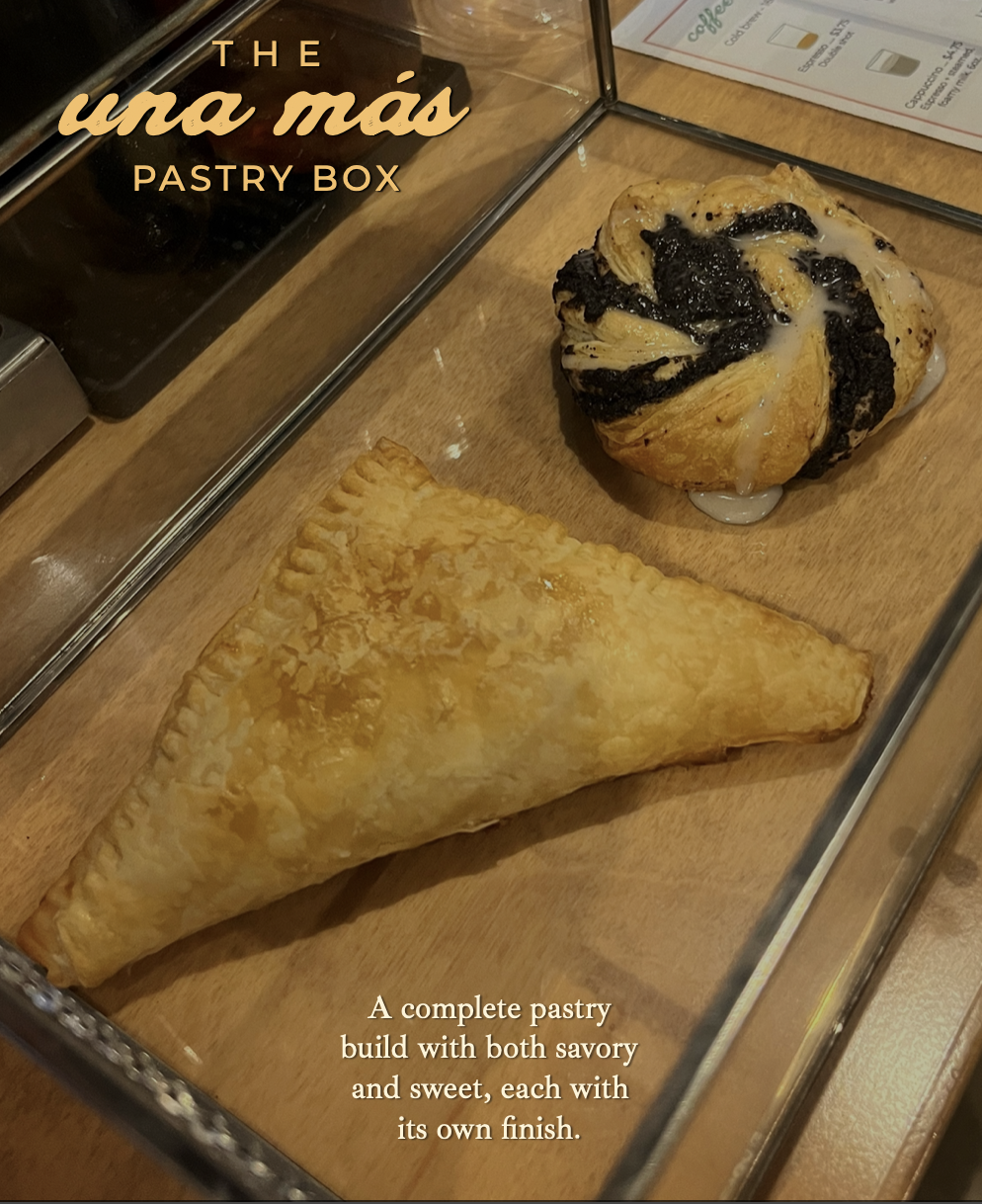 A pastry box containing a triangular, flaky, golden-brown savory turnover and a sweet pastry with a swirl of black fruit filling and sugar glaze, set on a wooden surface.