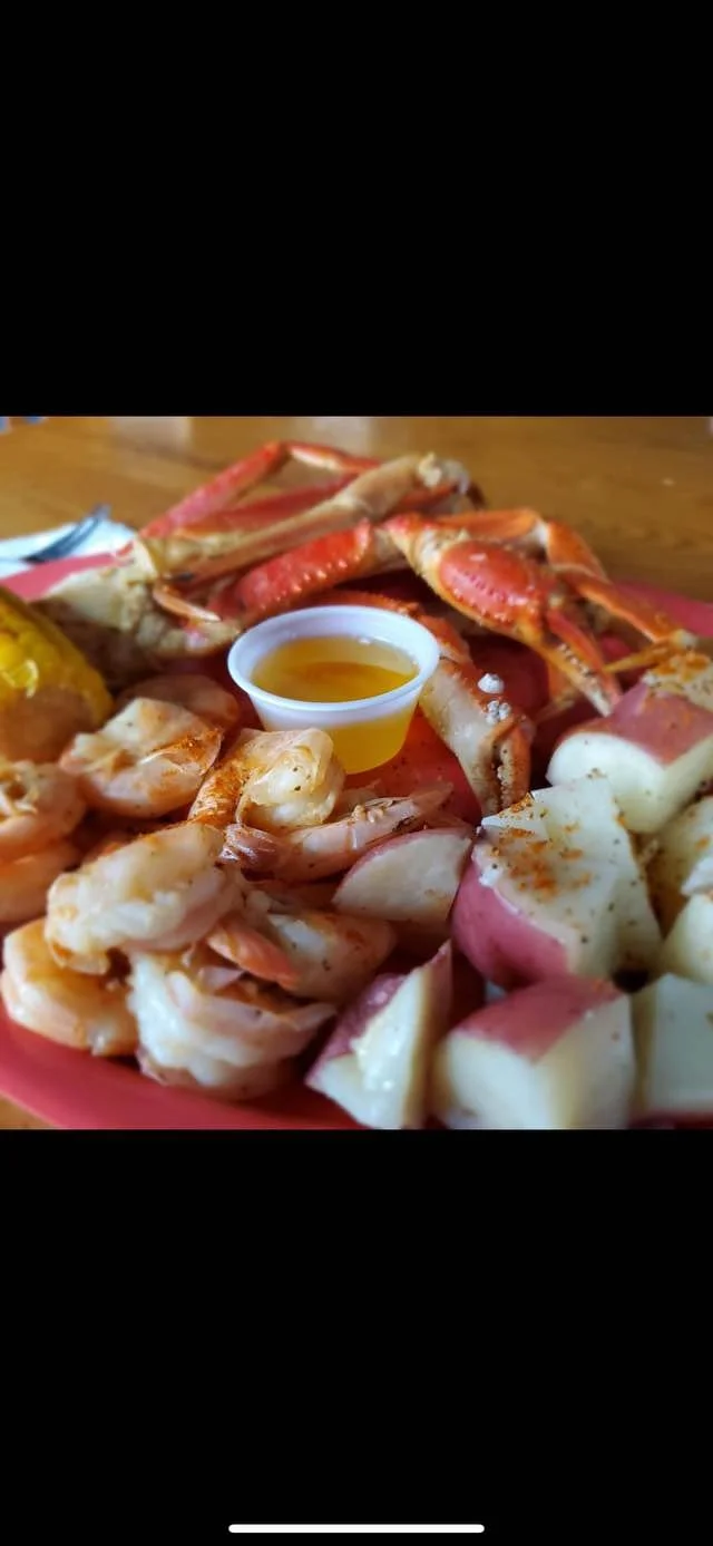 Seafood platter with lobster, shrimp, and pieces of fish, served with a small cup of dipping sauce, on a pink plate.