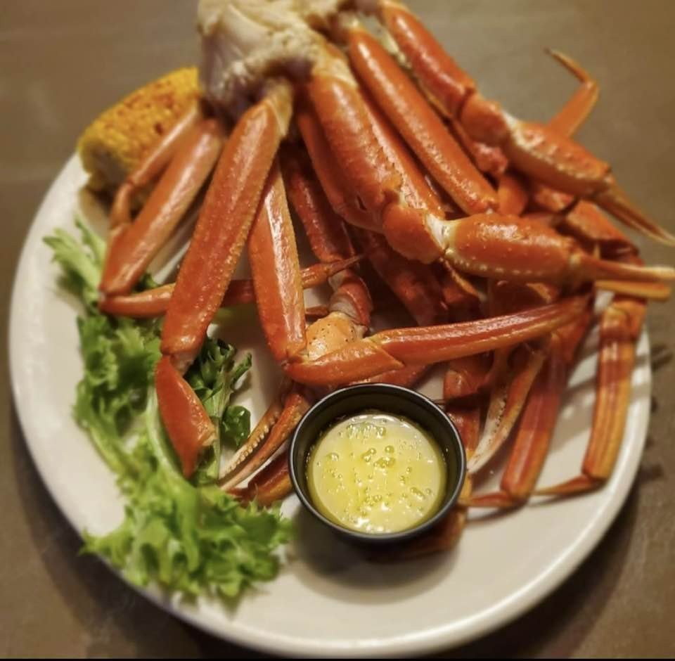 A plate of cooked snow crabs served with a small cup of melted butter and fresh greens.