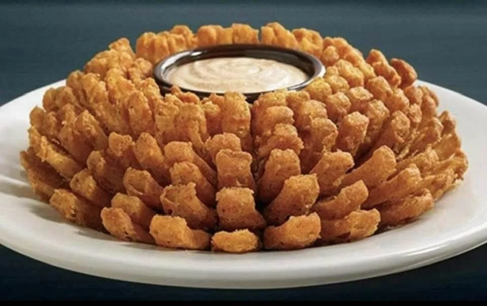 Fried onion ring display on a white plate with a small cup of dipping sauce in the center.