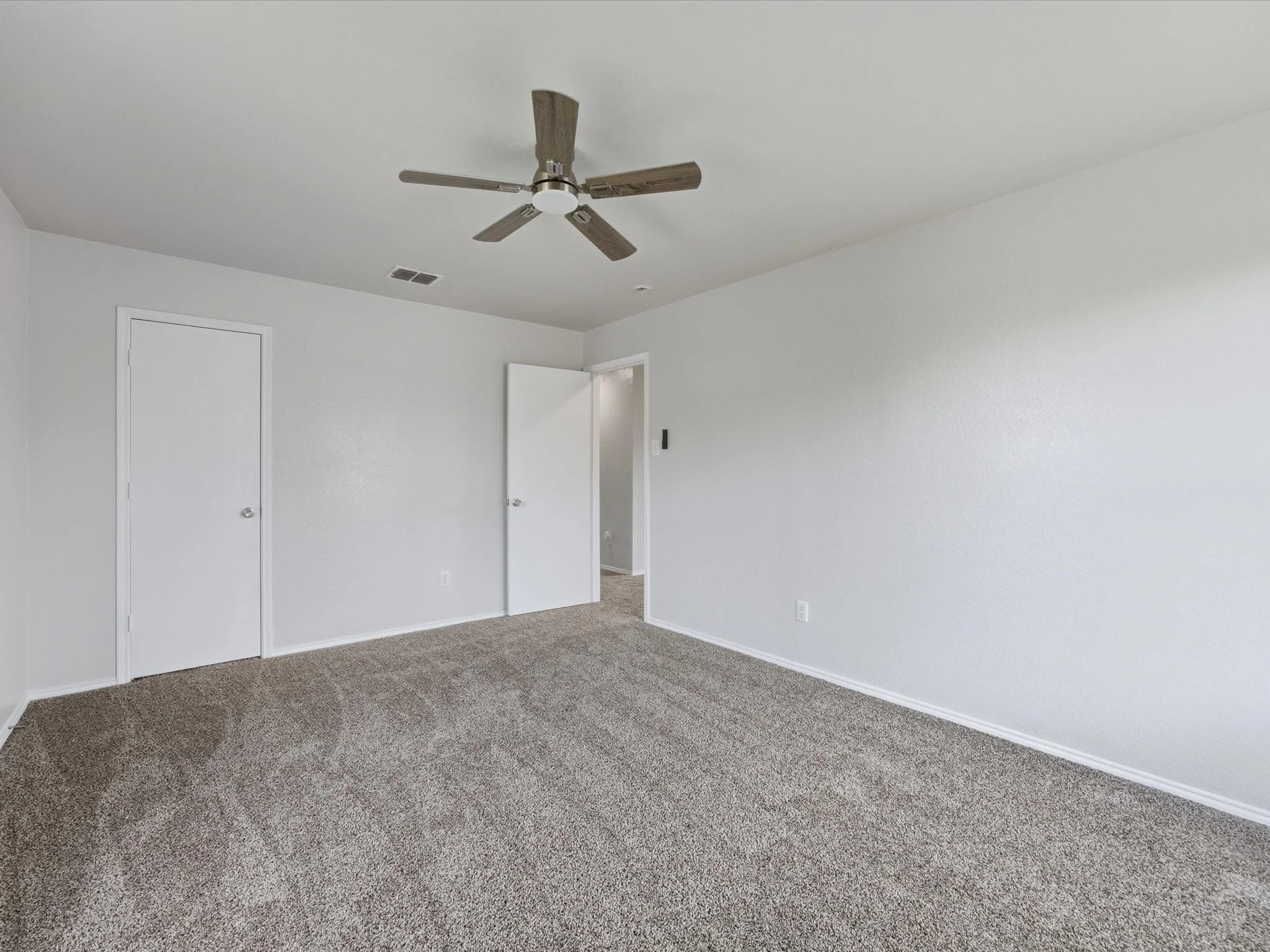 Empty room with white walls, a ceiling fan, a closed closet door, an open doorway, and brown carpeting.