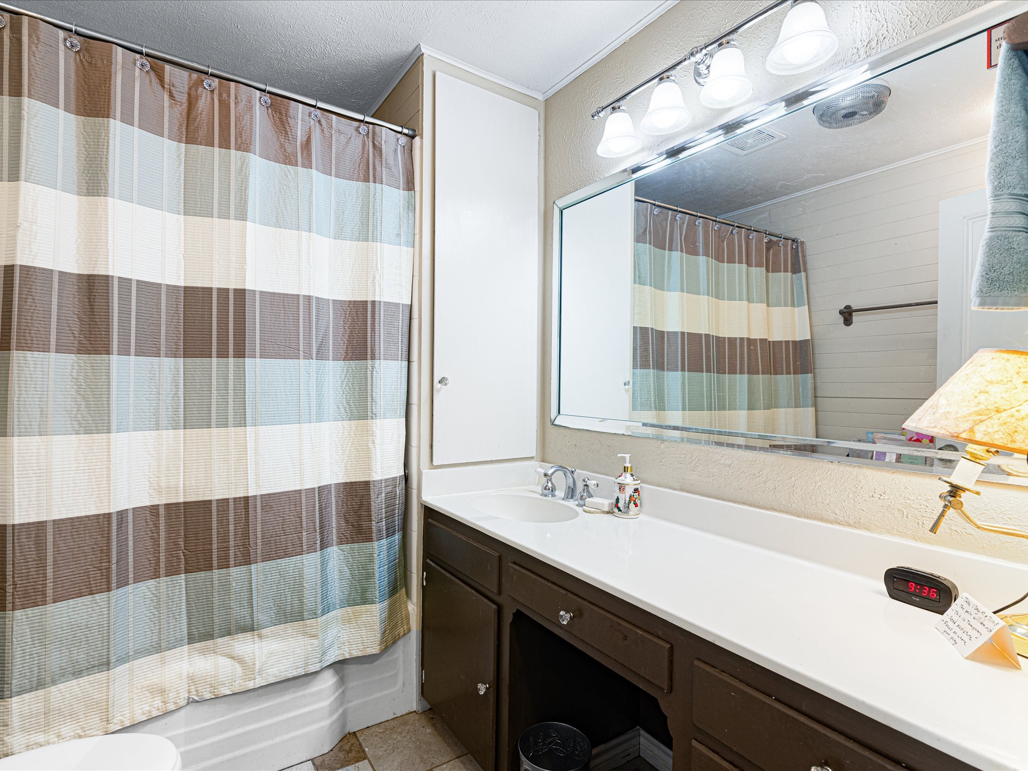 Bathroom with striped shower curtain, white sink, dark wood cabinet, mirror, and overhead lights.