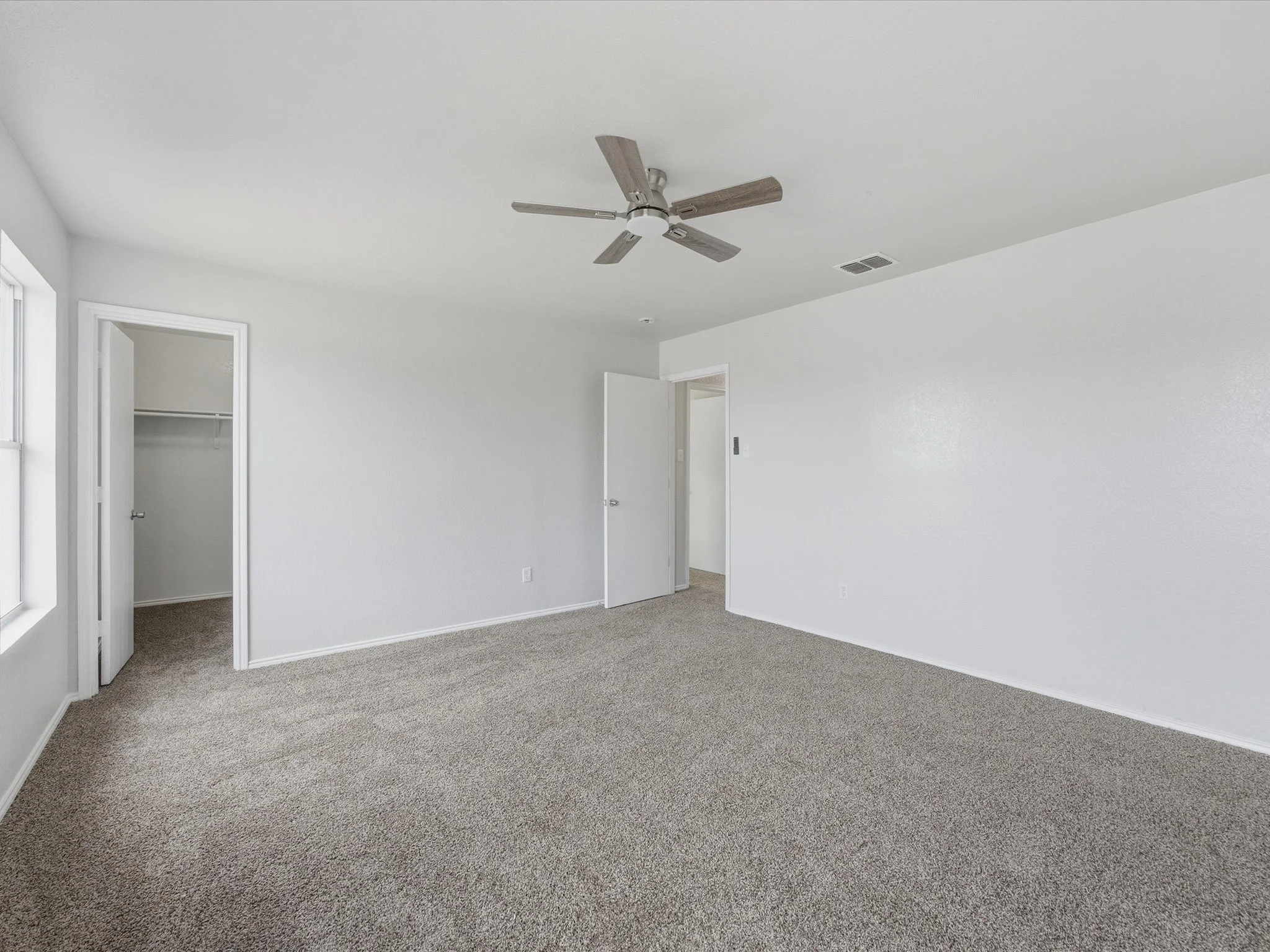 Empty bedroom with beige carpet, white walls, two open doors leading to closets or other rooms, and a ceiling fan.