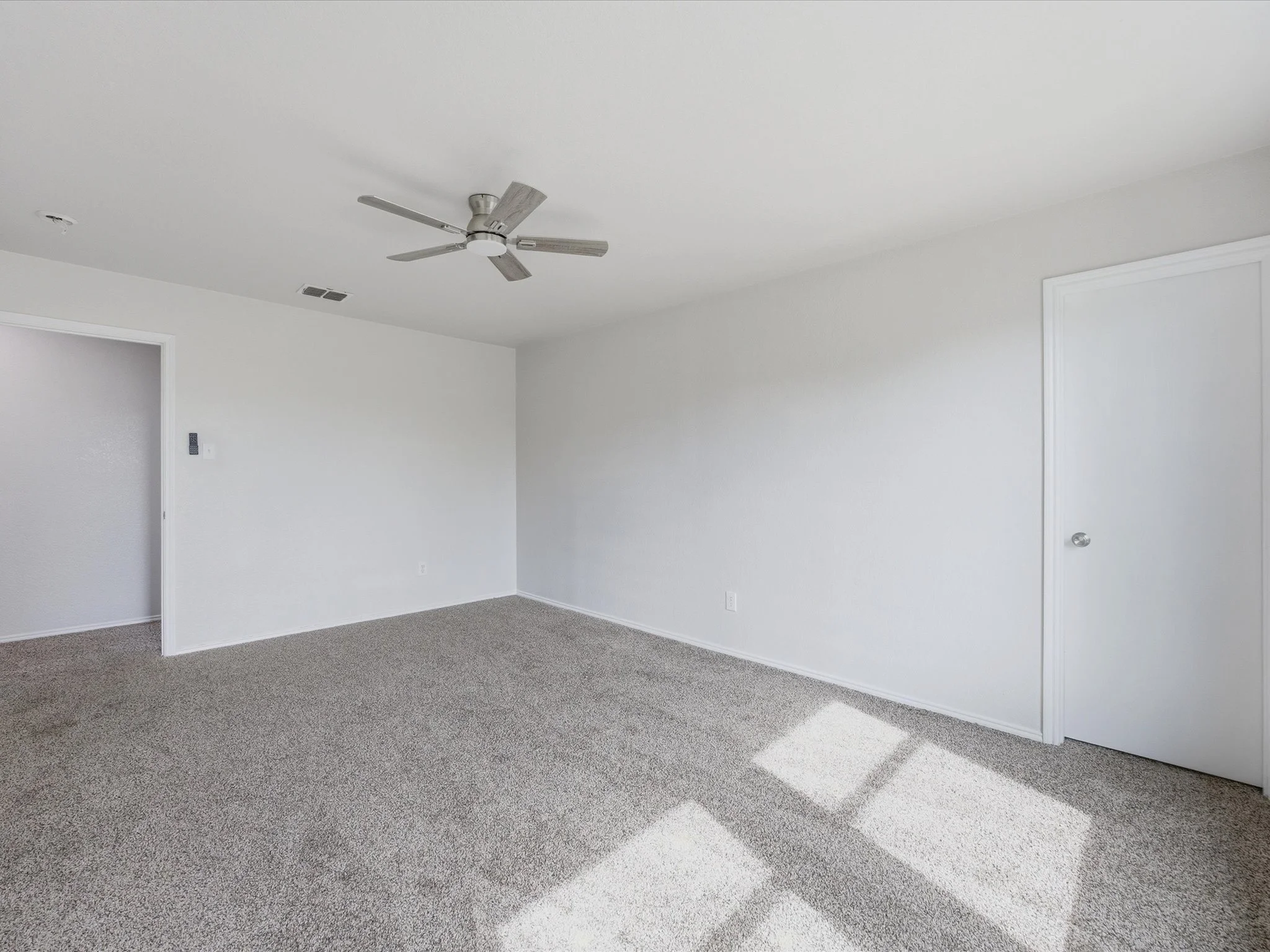 Empty white room with beige carpet, ceiling fan, and closed doors