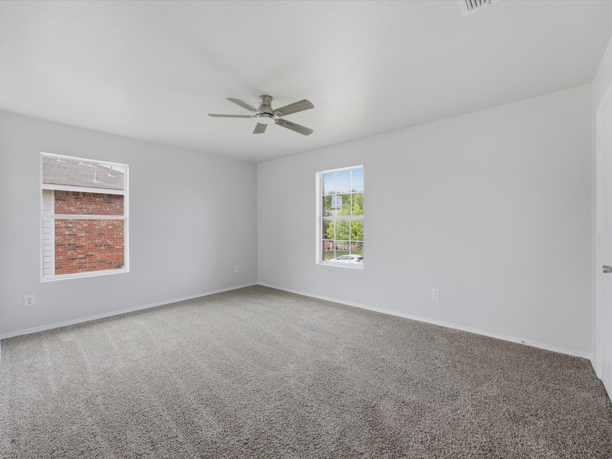 Empty room with light gray walls, two windows, beige carpet, and a ceiling fan.