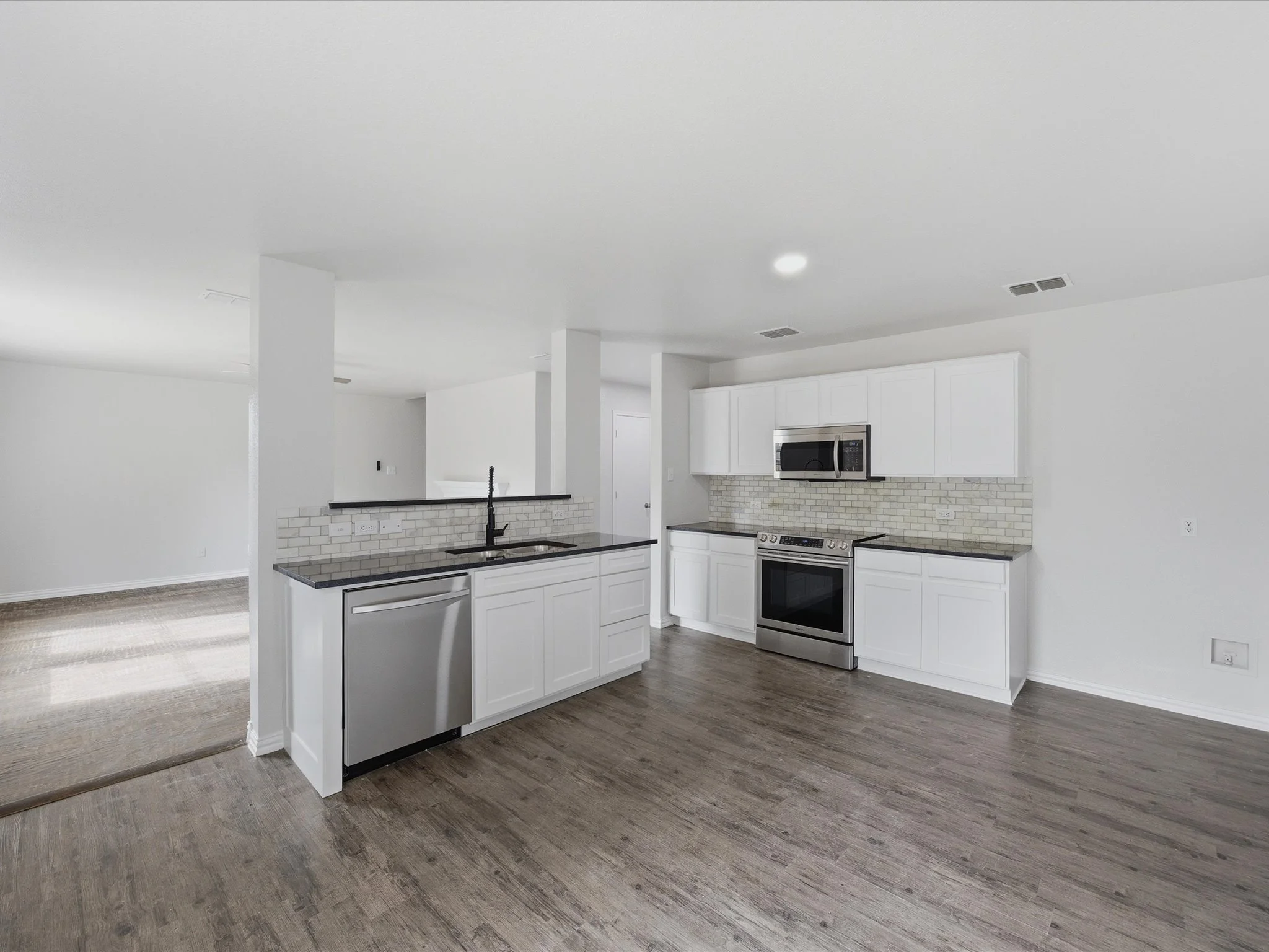 Modern white kitchen with island, stainless steel appliances, and wood flooring.