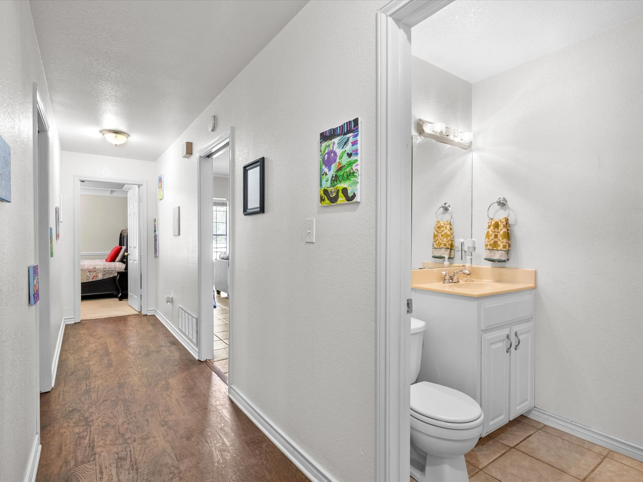 Hallway leading to a bedroom on the left and a bathroom on the right, with artwork on the walls and a ceiling light.
