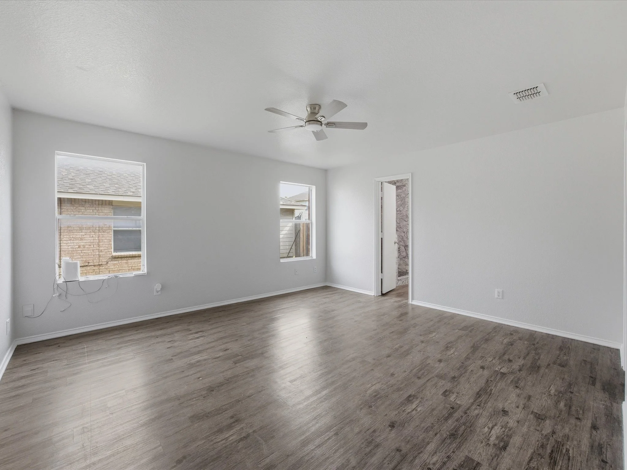 Empty room with white walls, a ceiling fan, two windows, and brown wood flooring.