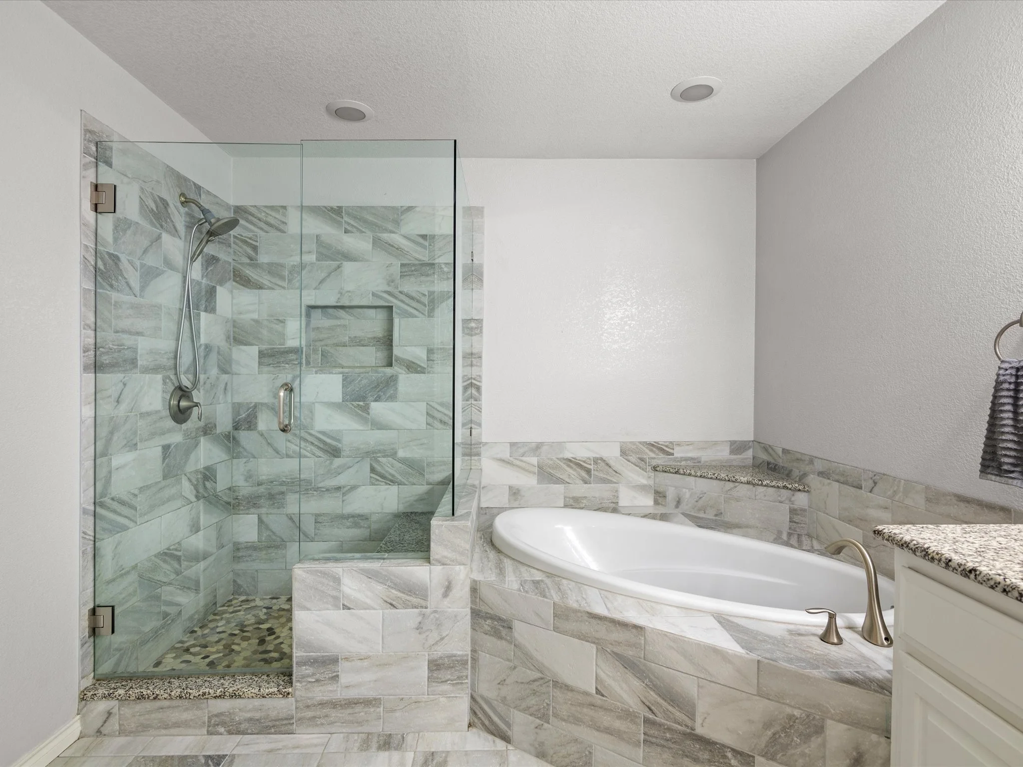 A bathroom with a shower enclosure and a bathtub, featuring marble tiles, a granite countertop, and a towel hanging on a metal rod.