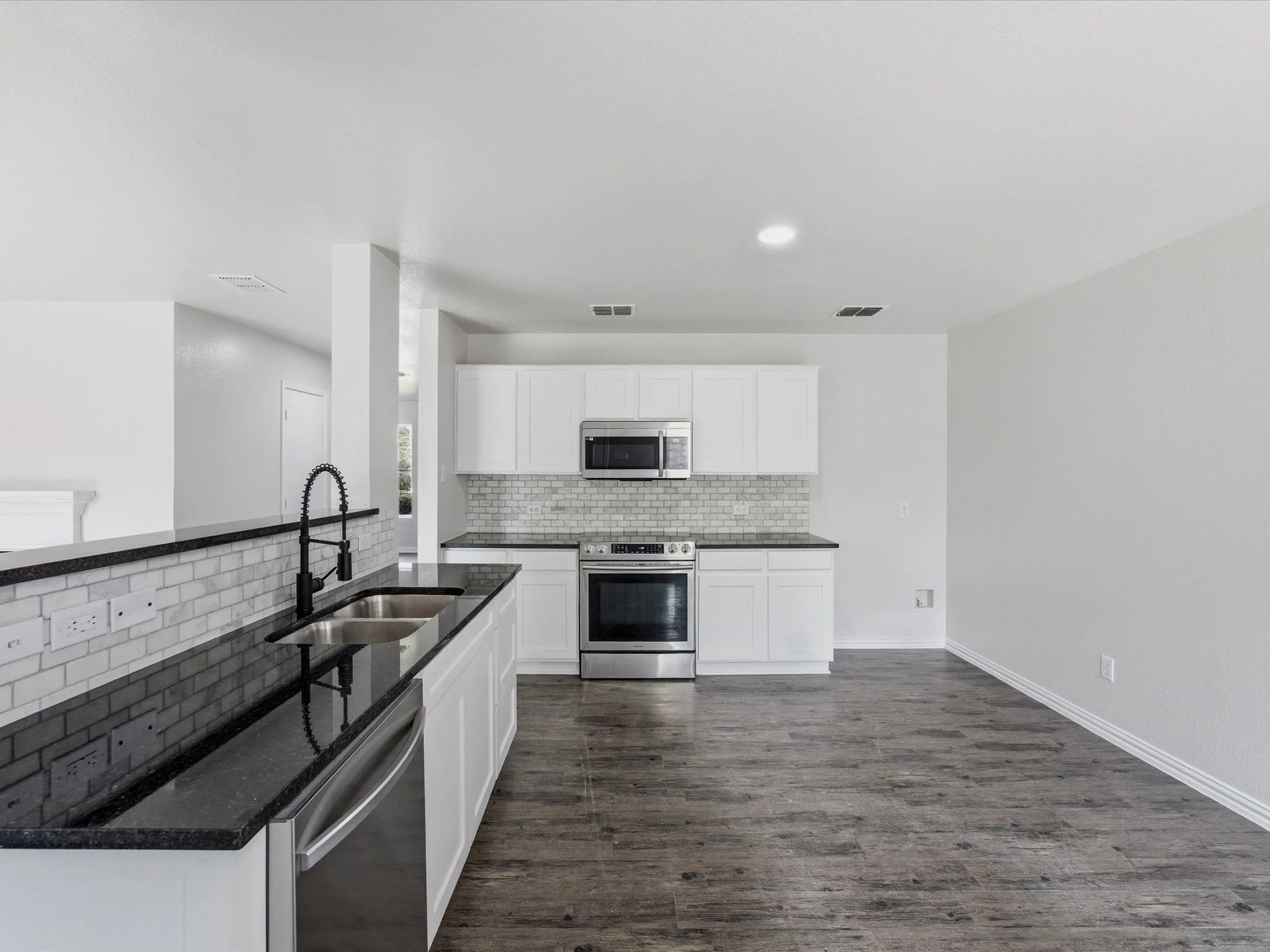 Modern kitchen with white cabinets, stainless steel appliances, black countertops, a black faucet, and wood flooring.
