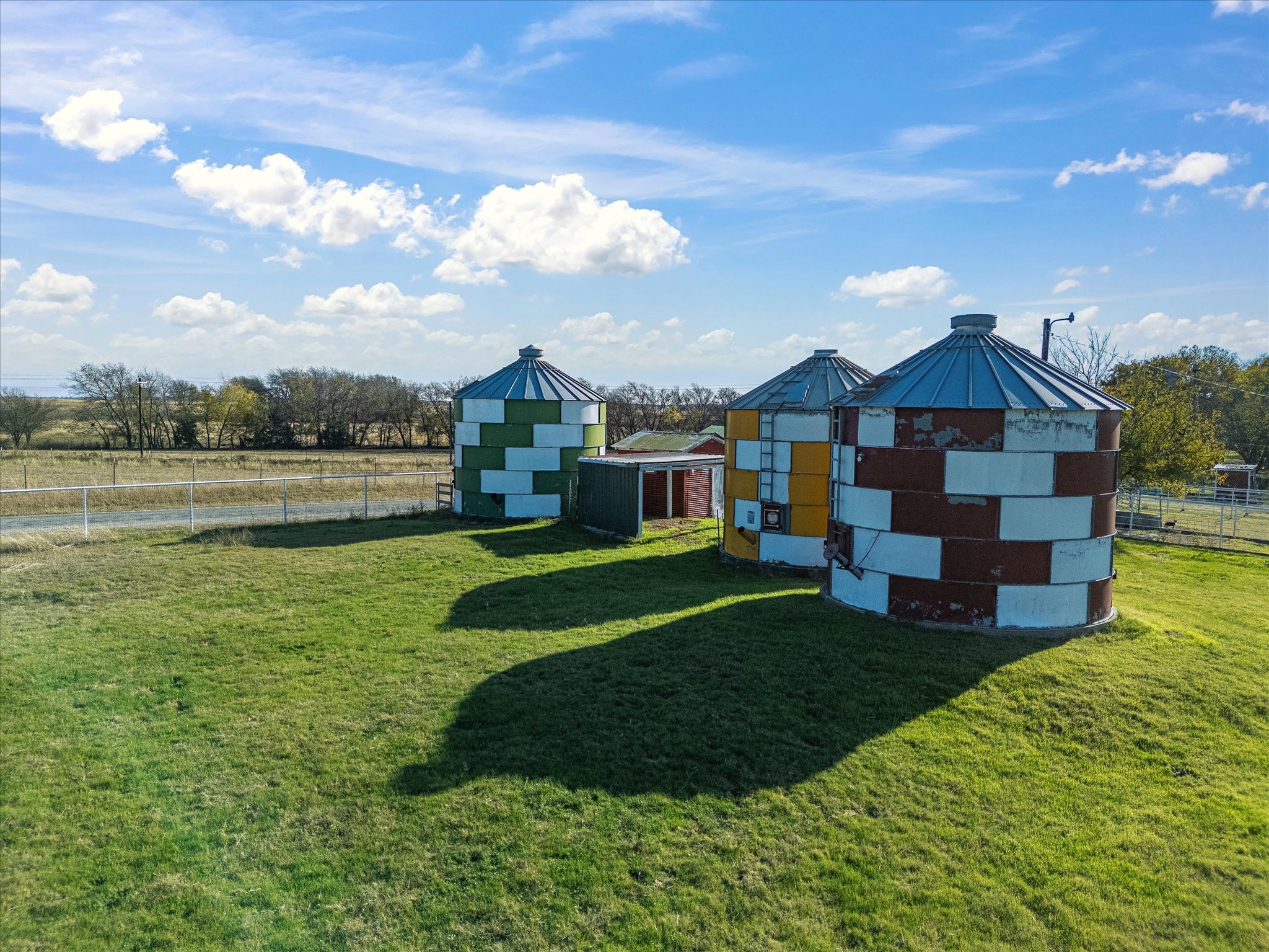 Colorful cylindrical structures with conical metal roofs in a grassy outdoor area under a partly cloudy sky.