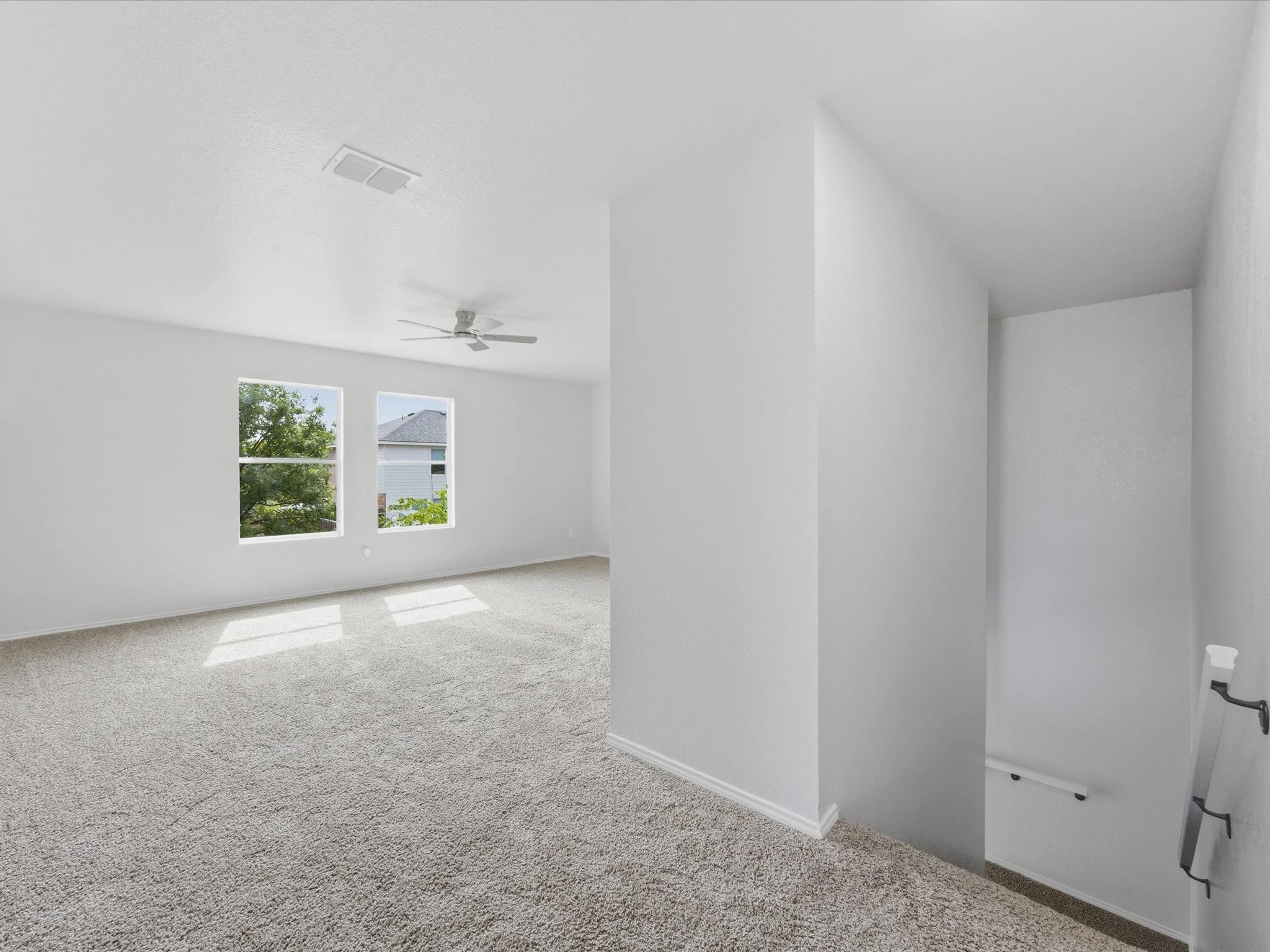Empty white room with gray carpet, two windows, ceiling fan, and electrical outlet.