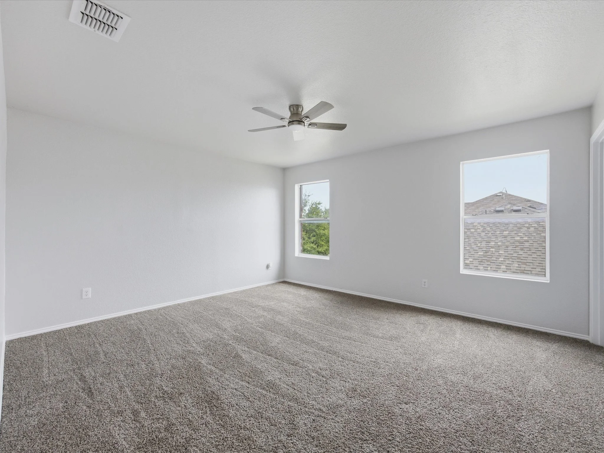 Empty bedroom with white walls, a ceiling fan, two windows, and gray carpet.