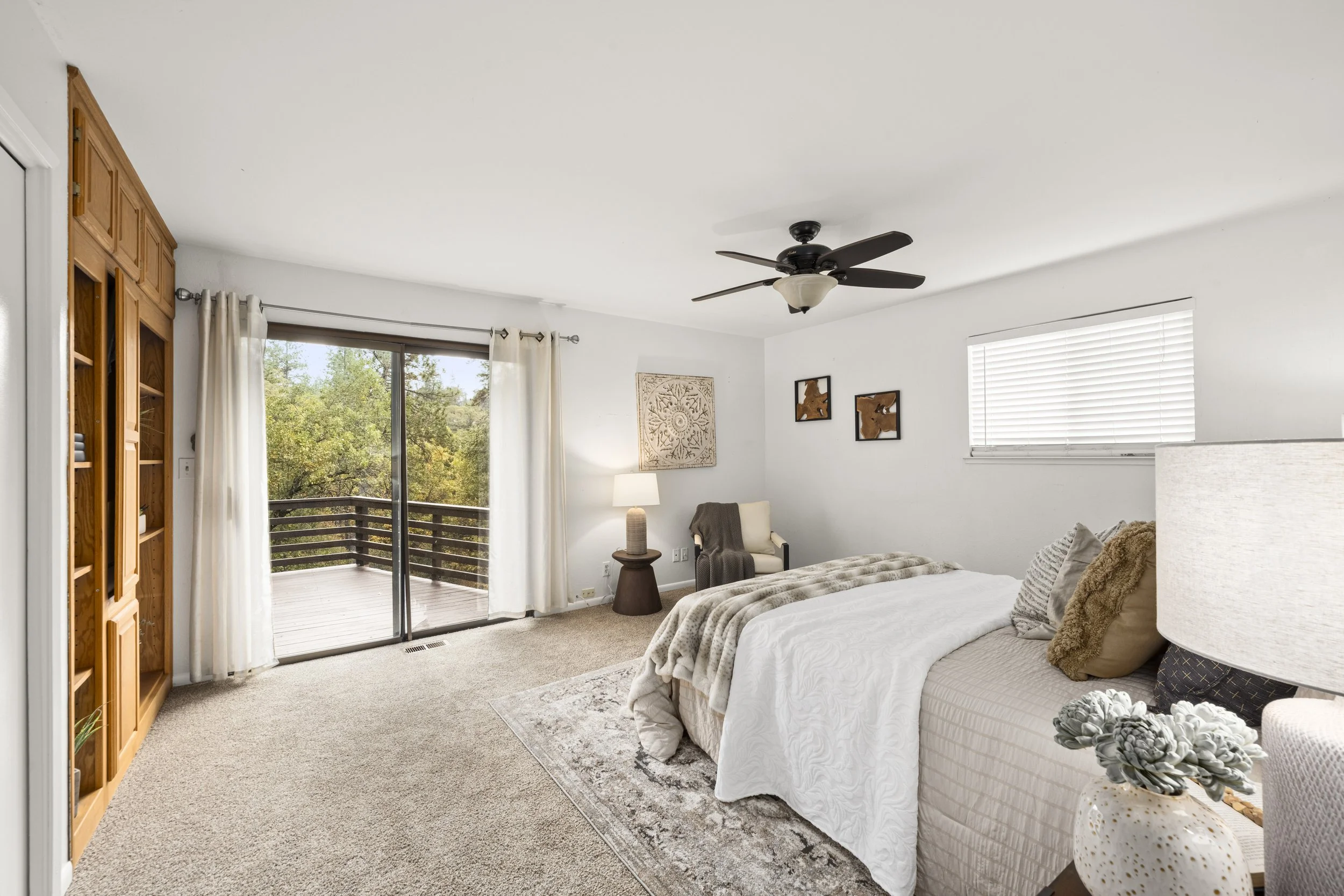 A bedroom with a sliding glass door leading to a balcony, a ceiling fan, a bedside lamp, and a bed with pillows and a blanket.