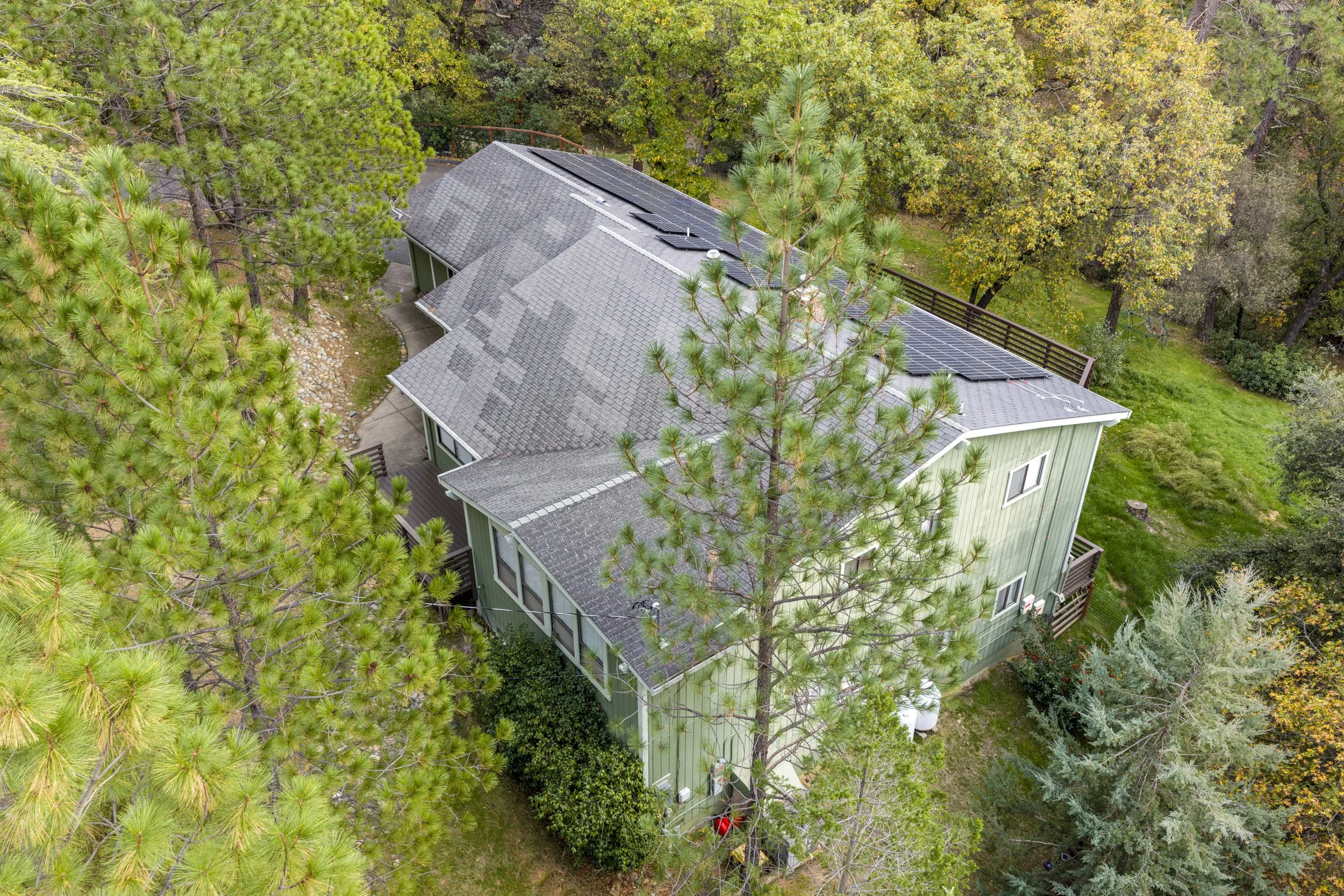 An aerial view of a house with a rooftop covered in solar panels, surrounded by dense green trees and foliage.