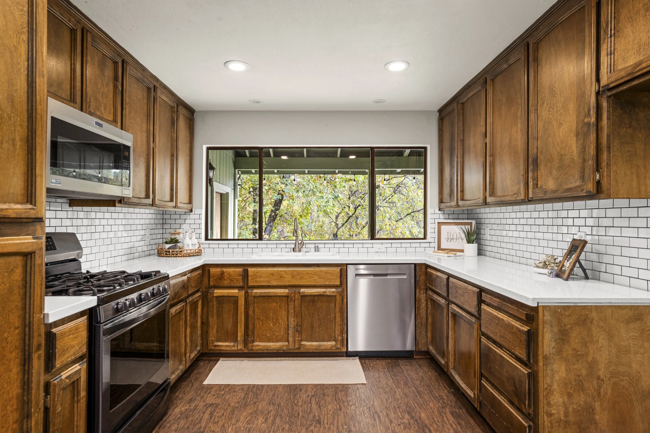 Kitchen with dark wood cabinets, white subway tile backsplash, stainless steel appliances, and a large window with trees outside.