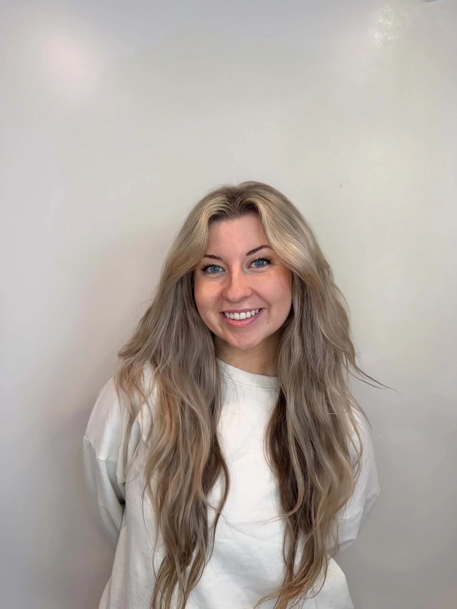 A young woman, with dirty blonde hair standing in front of a white wall