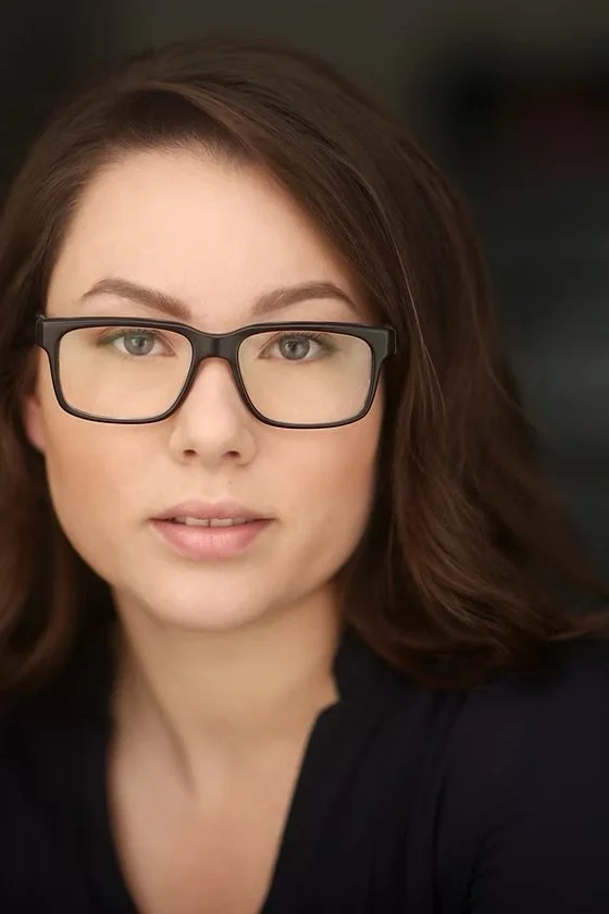 A woman with brown hair and glasses looking directly at the camera.