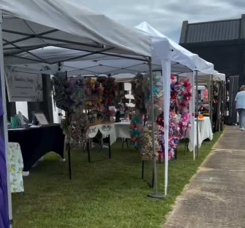 Outdoor market booth with white canopy selling floral and decorative wreaths and arrangements.