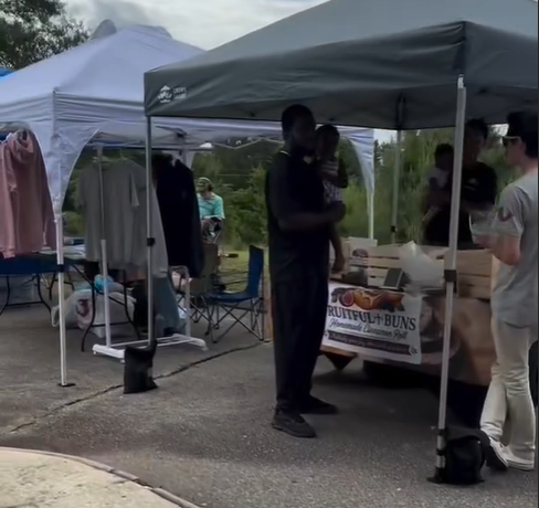 People at an outdoor market stall with tents and clothing on display.