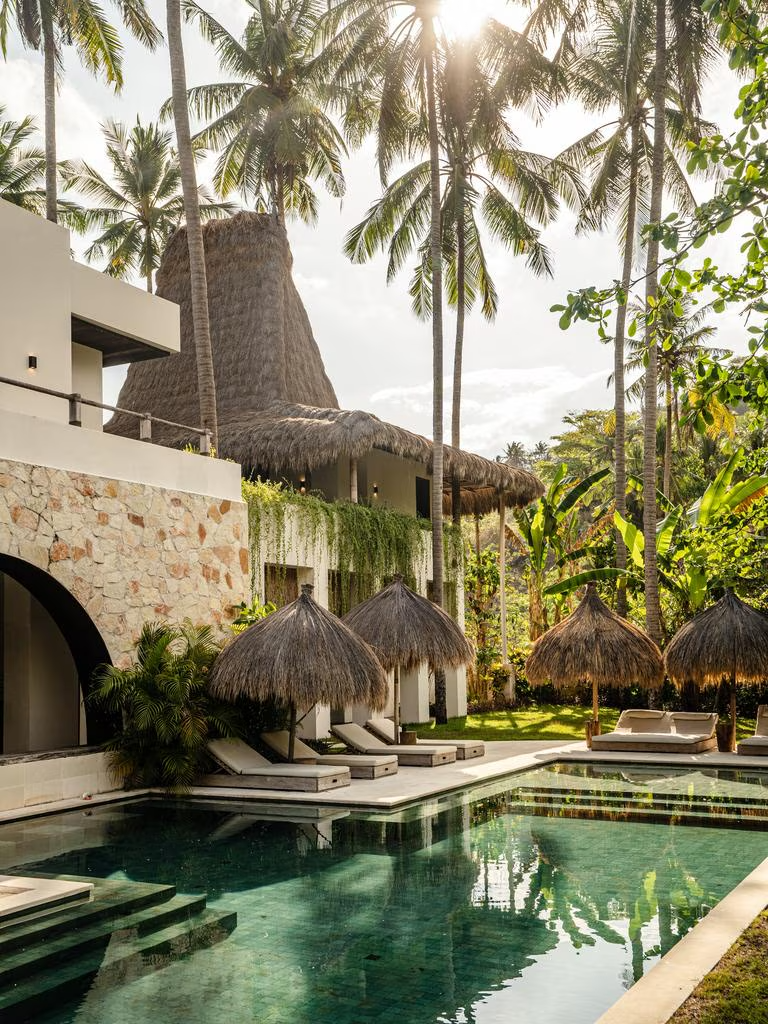 Luxury Bali yoga retreat accommodation with thatched roof villa surrounded by palm trees and private pool ideal for pilates wellness holiday