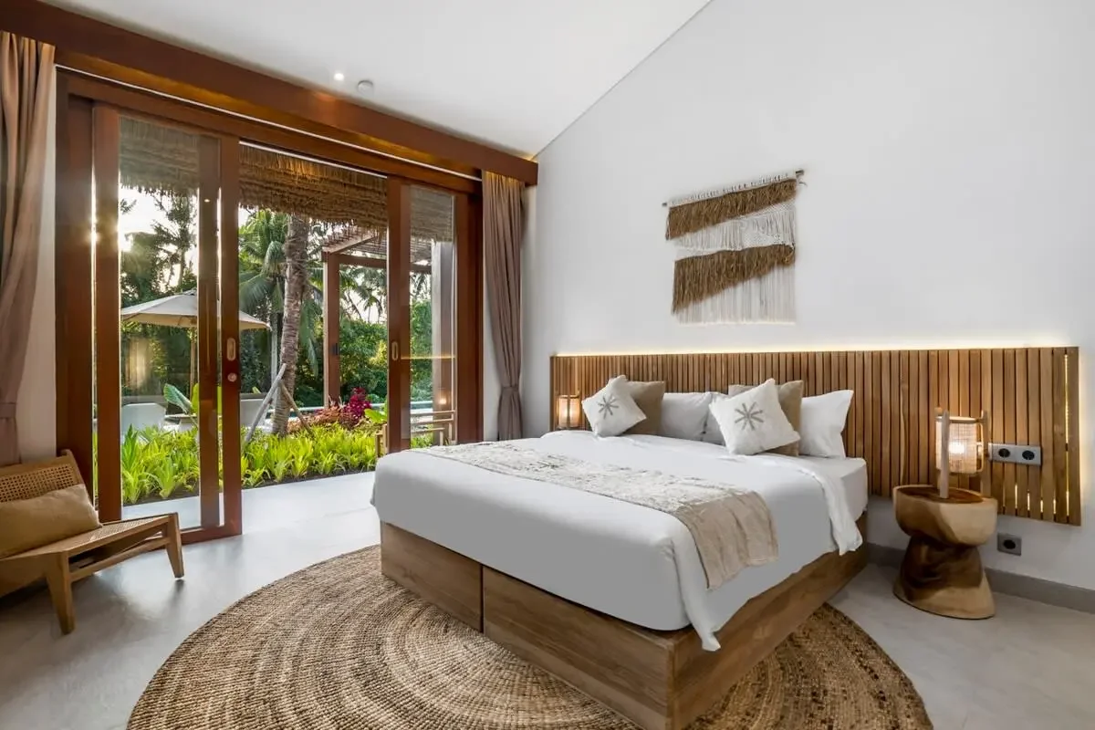 Contemporary bedroom with wooden accents, sliding glass doors opening to greenery, bed with beige and white pillows, woven wall hanging, and natural decor.