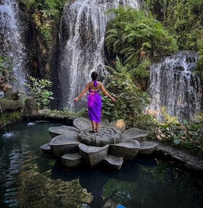 Woman in purple standing beneath a lush jungle waterfall in Bali