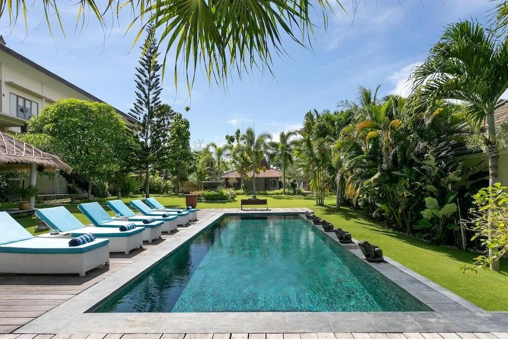 Luxury outdoor swimming pool surrounded by palm trees and lounge chairs on a wooden deck.