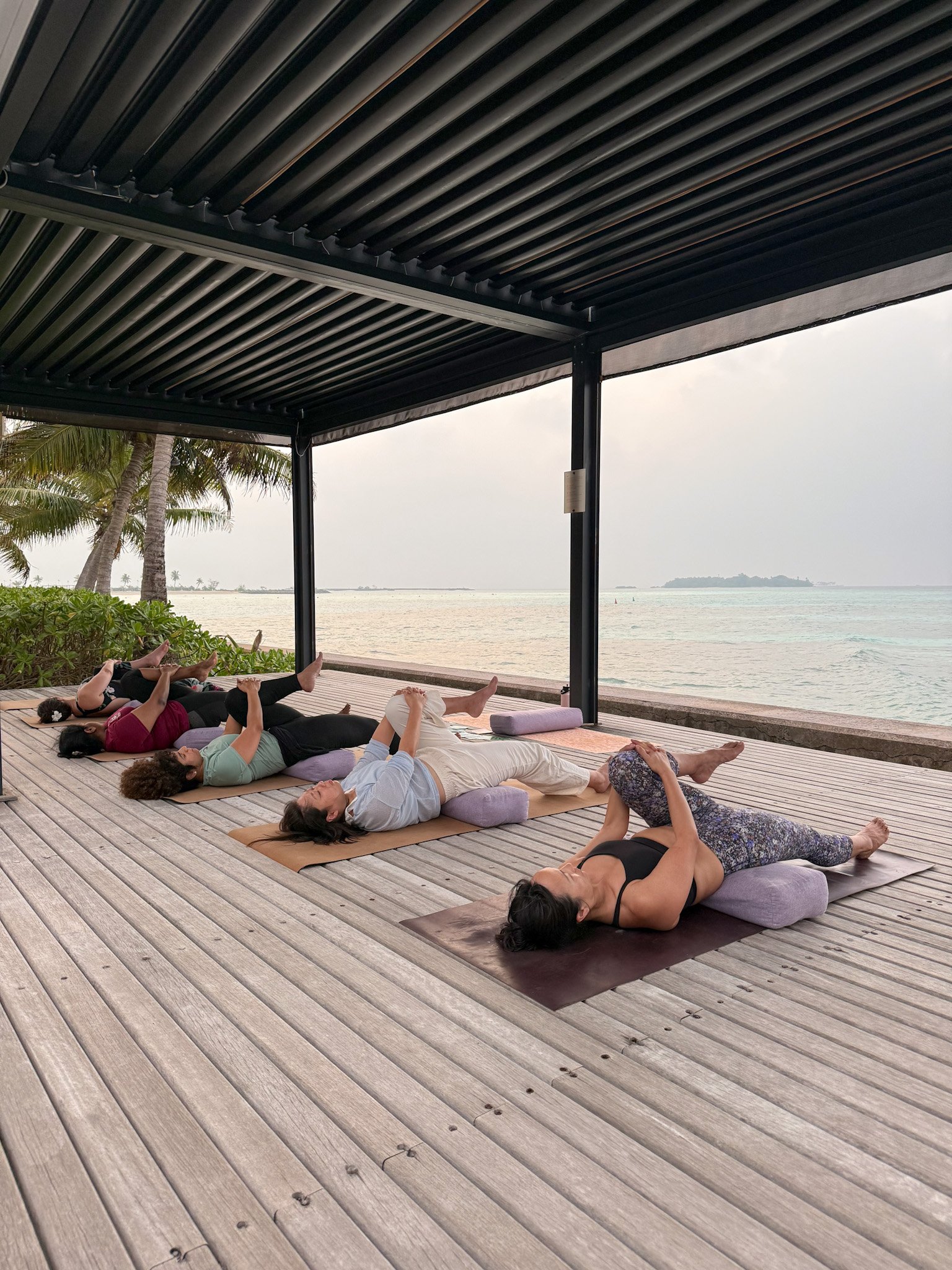 Group pilates class on overwater deck overlooking the Indian Ocean, Maldives wellness retreat