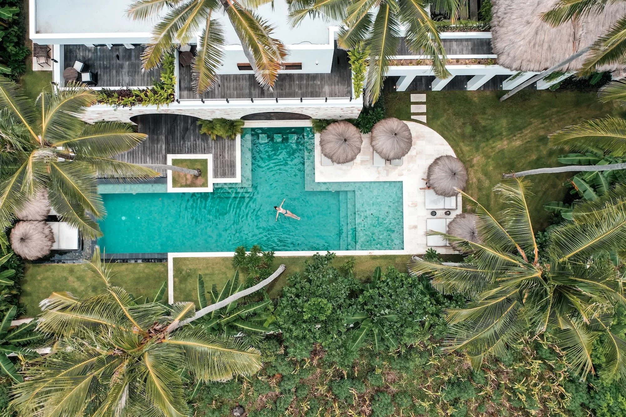 Aerial view of luxury retreat pool with thatched umbrellas at Bali yoga and pilates resort Indonesia tropical garden setting