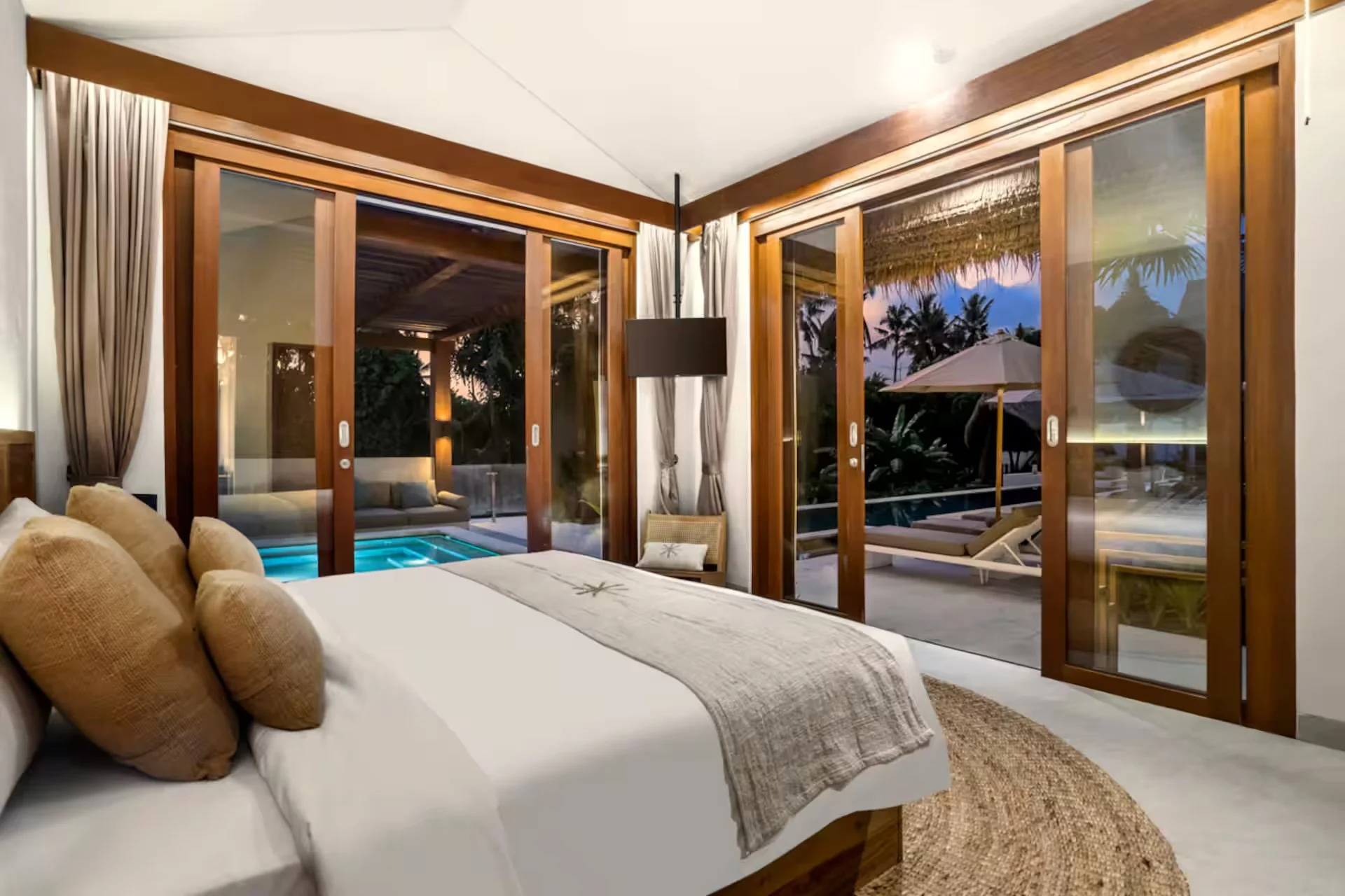 Luxury bedroom at Bali yoga pilates retreat Indonesia with sliding glass doors opening to private outdoor terrace and tropical sunset view