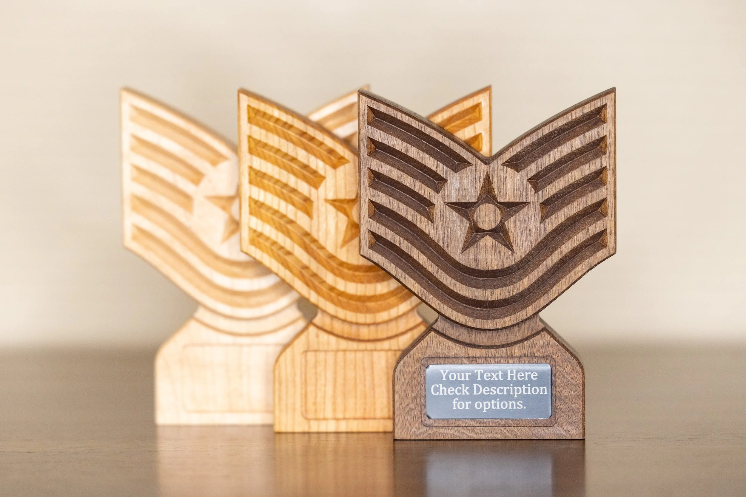 Close-up of three wooden awards or trophies with baseball cap designs, one darker and two lighter, on a dark surface with a plain background.