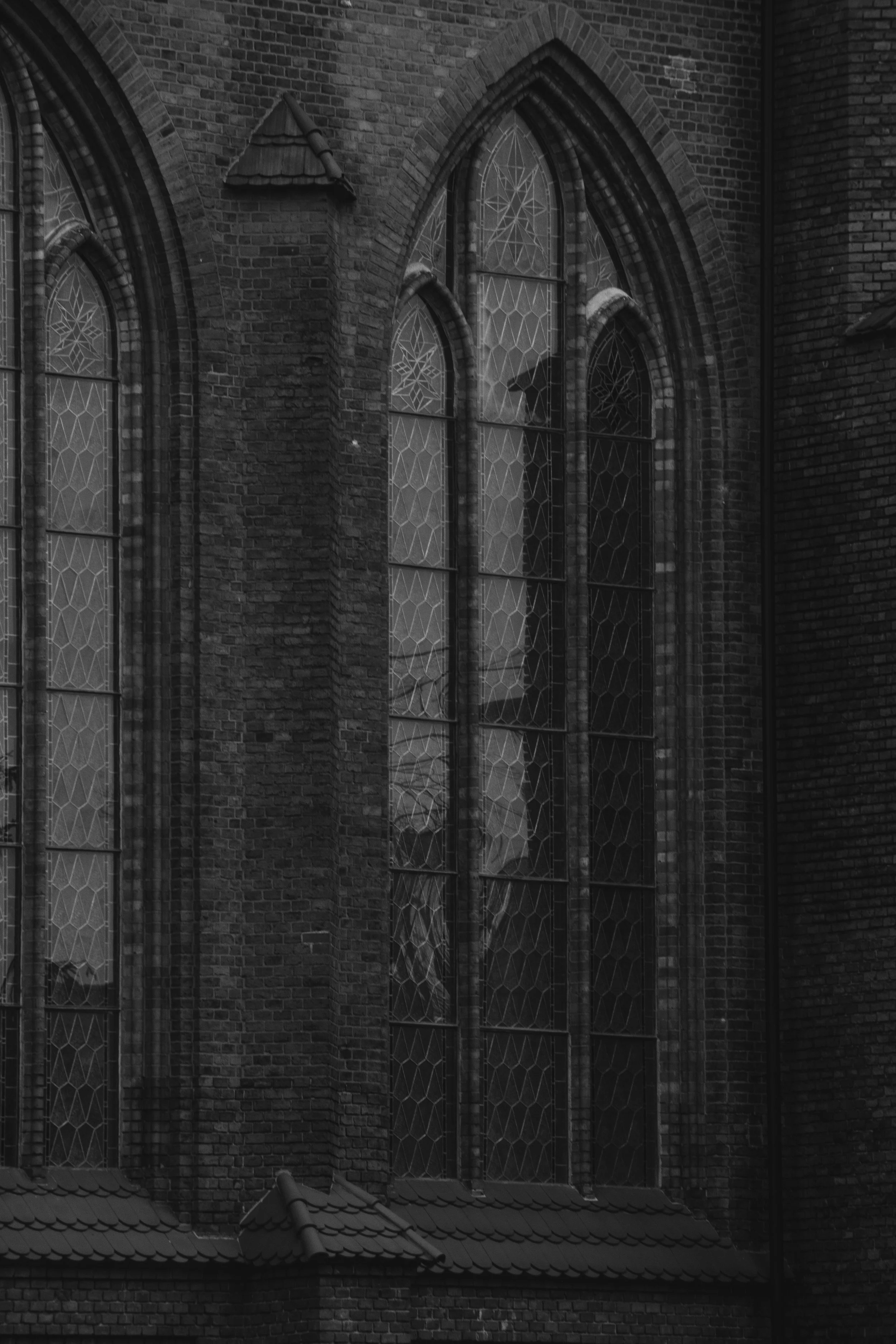 Black and white photograph of a church exterior with pointed gothic windows featuring decorative stained glass and brick walls.