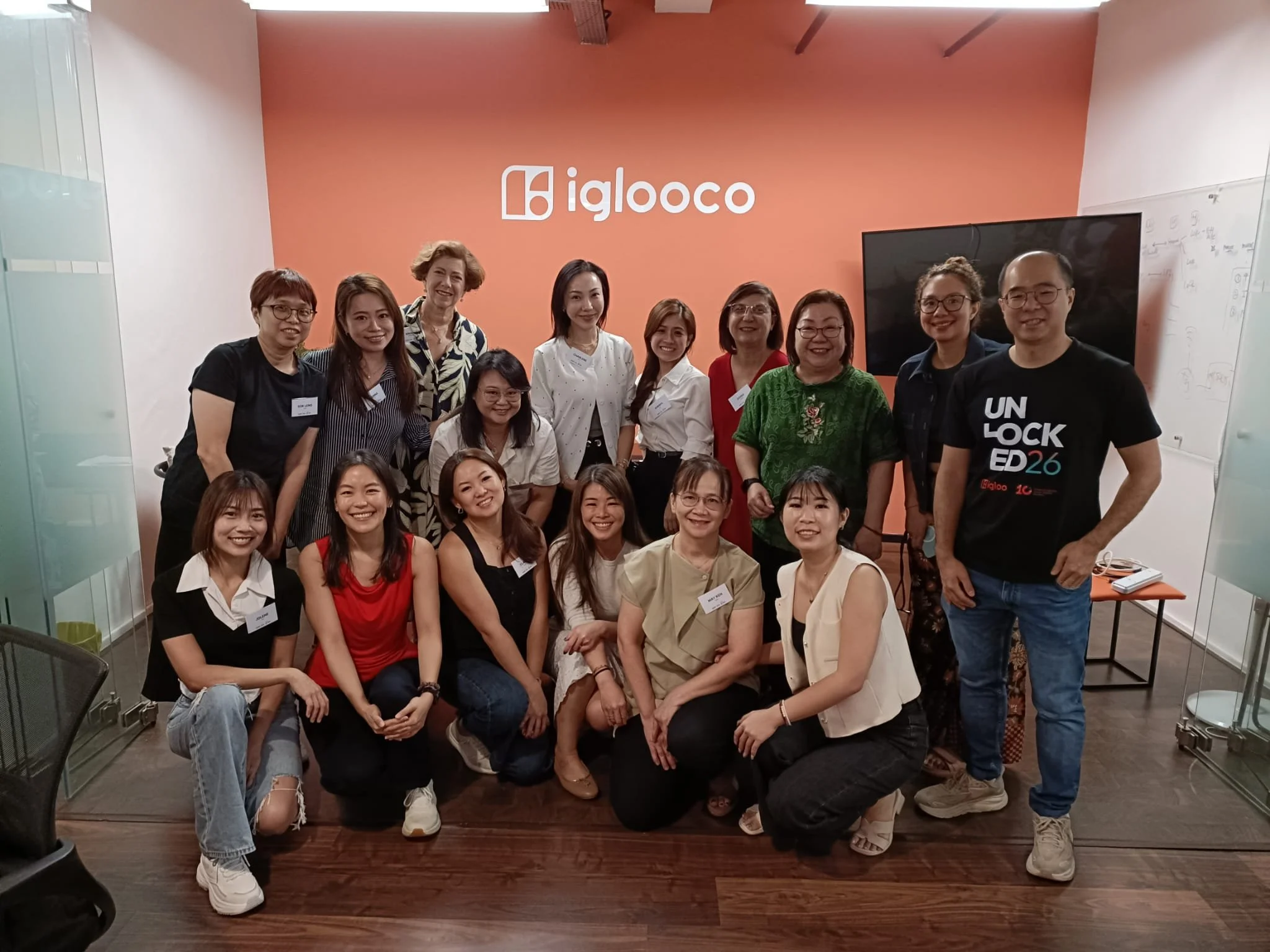 A group of people posing for a photo in a room with an 'iglooco' sign on the wall behind them. They are smiling and appear to be at an event or gathering.