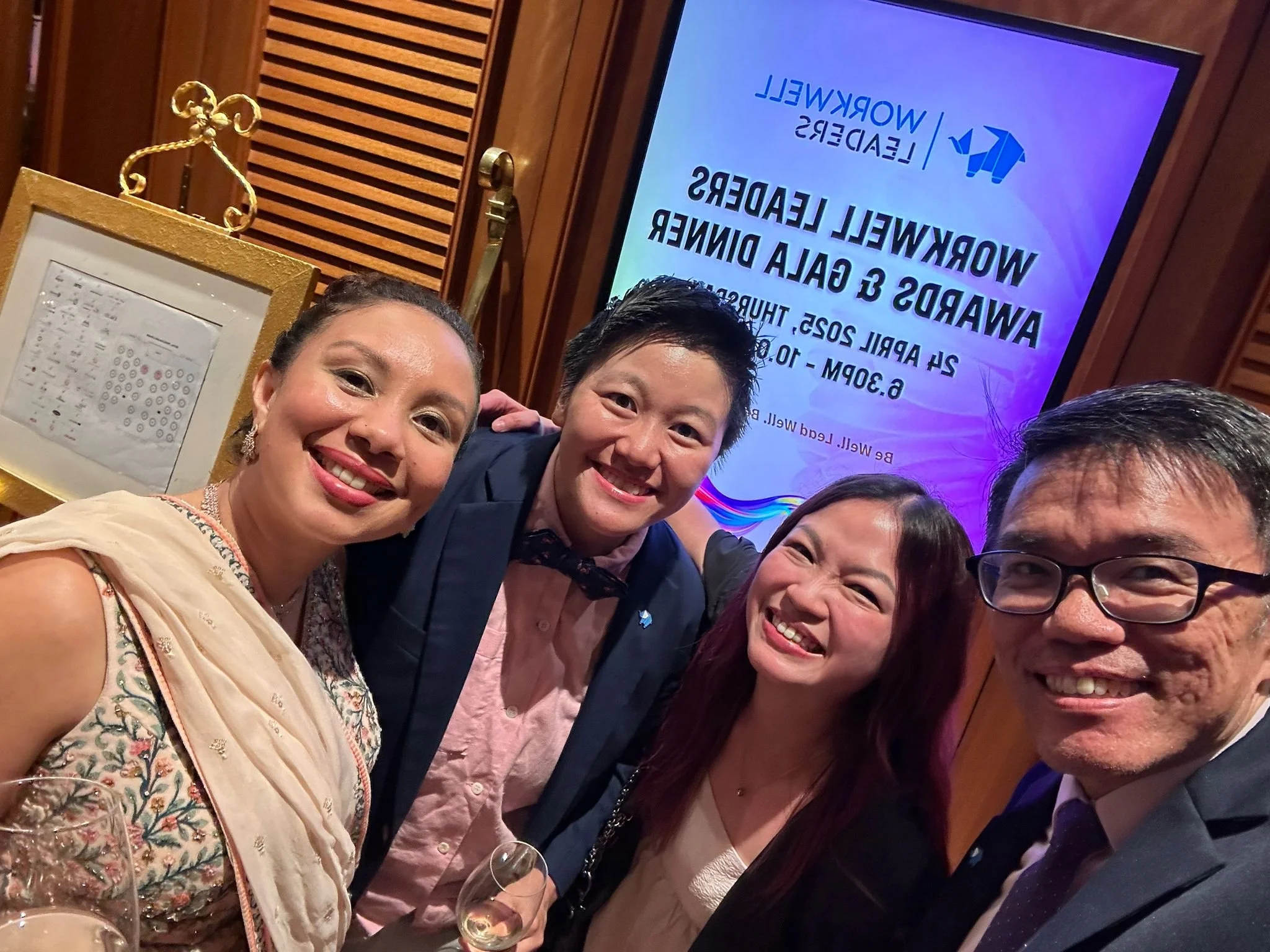 Group of people smiling and taking a selfie at a formal event in front of a screen displaying a message about awards leaders and a dinner event.