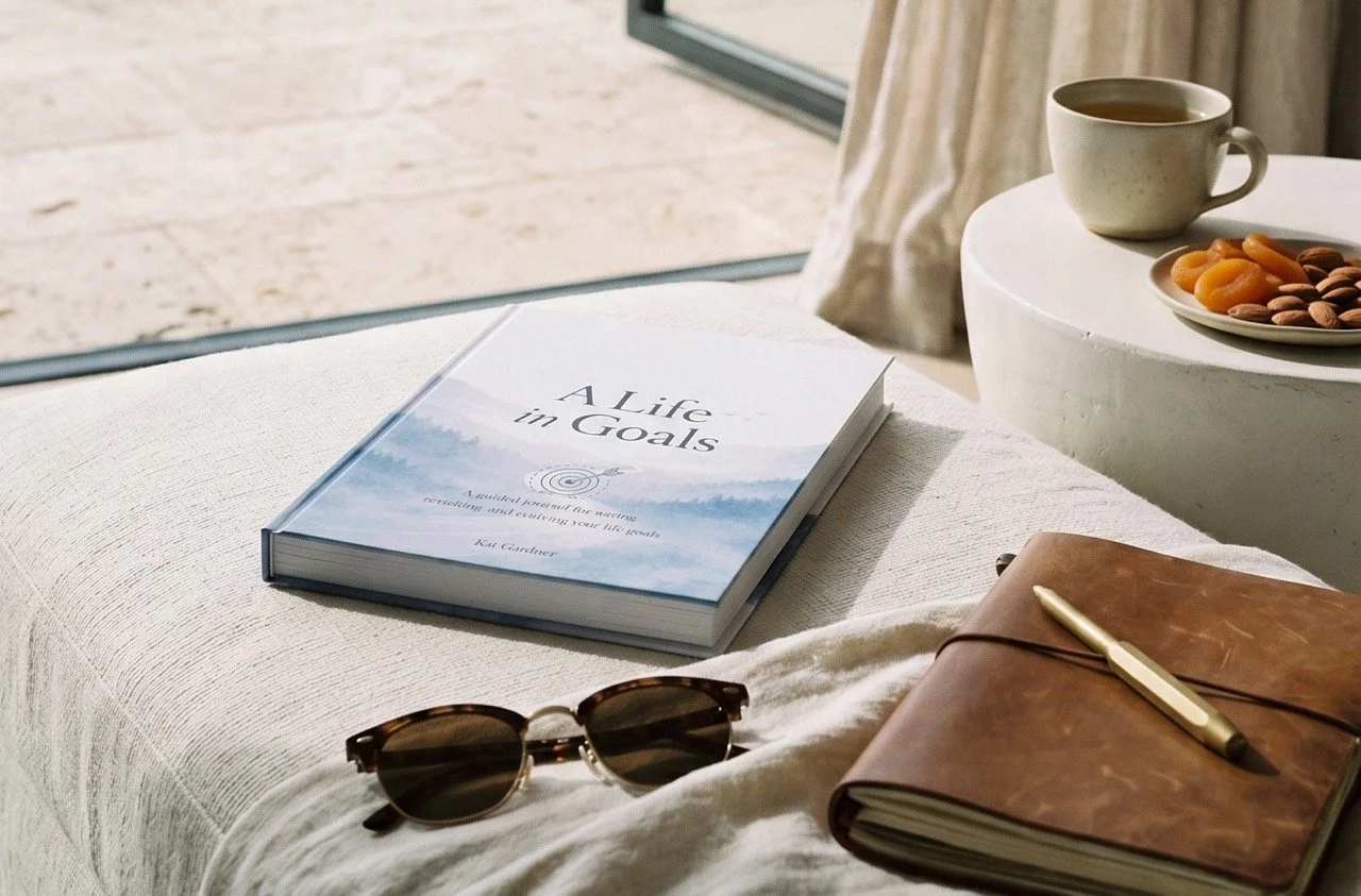 A Life in Goals guided journal with notebook, pen and sunglasses in a relaxed coastal setting, representing time to reflect on life goals and future plans.