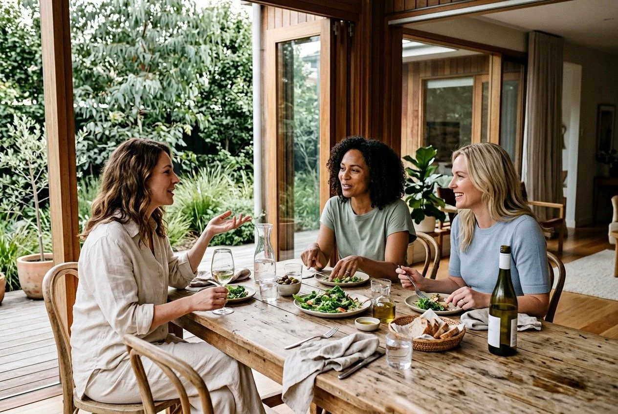Three women sharing a relaxed meal and conversation at home, representing friendship, relationships and making time for the people who matter.