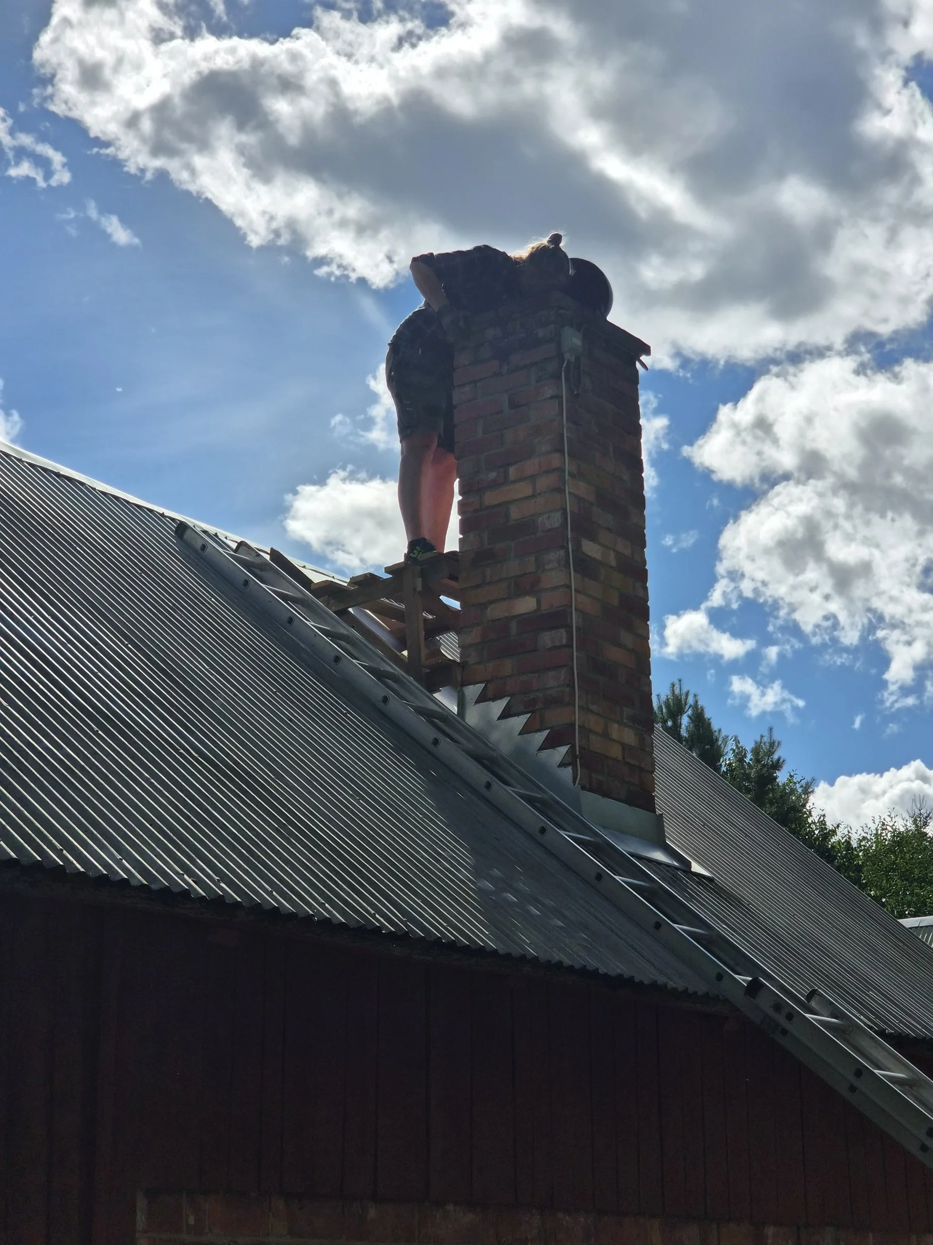 Person vid smedjans skorsten, sotar och sätter gnistgaller runt fläkten