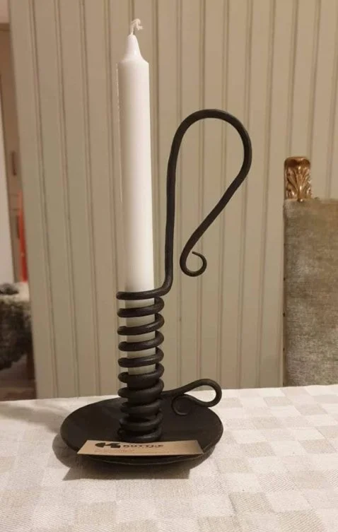 En svart ljusstake med en spiralformad design som håller ett vitt stearinljus, placerad på ett bord.
