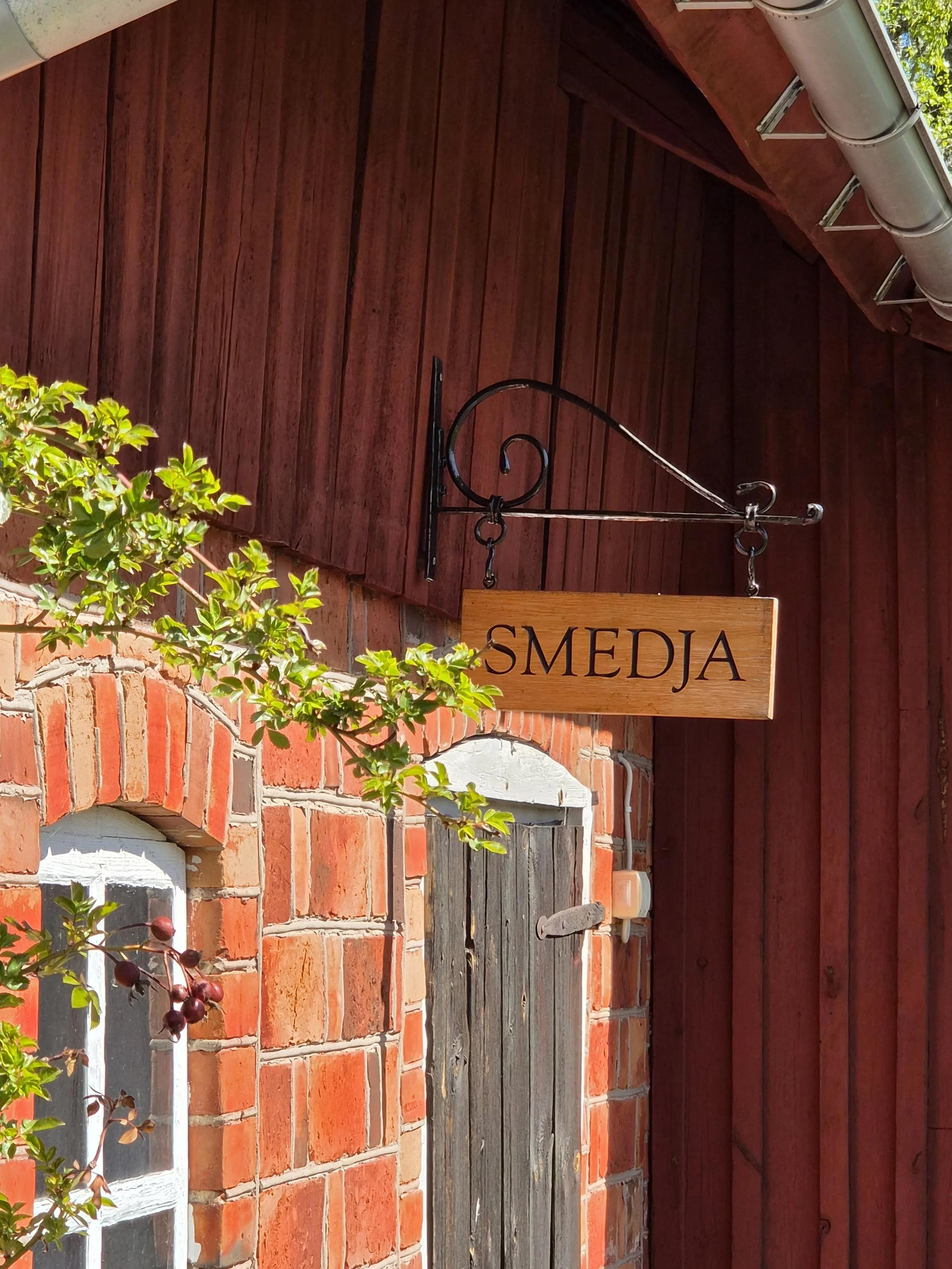 Bilden visar en skylt med texten smide. Skylten sitter på en gammal tegebyggnad