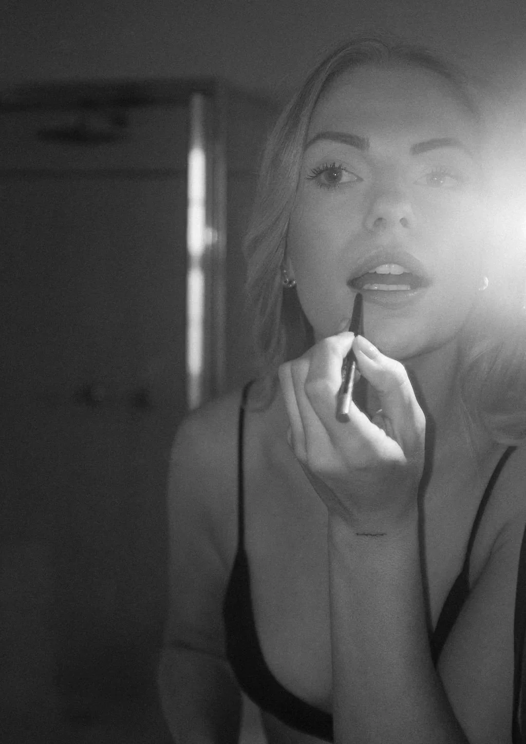 Black and white photo of a woman applying lipstick in front of a mirror.