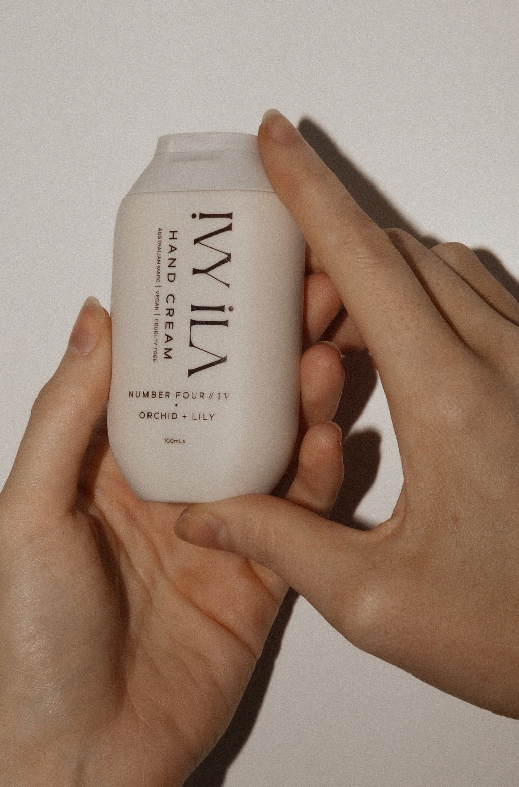 A person's hand holding a white can of MY iLIA hand cream with minimalistic black text and a plain background.