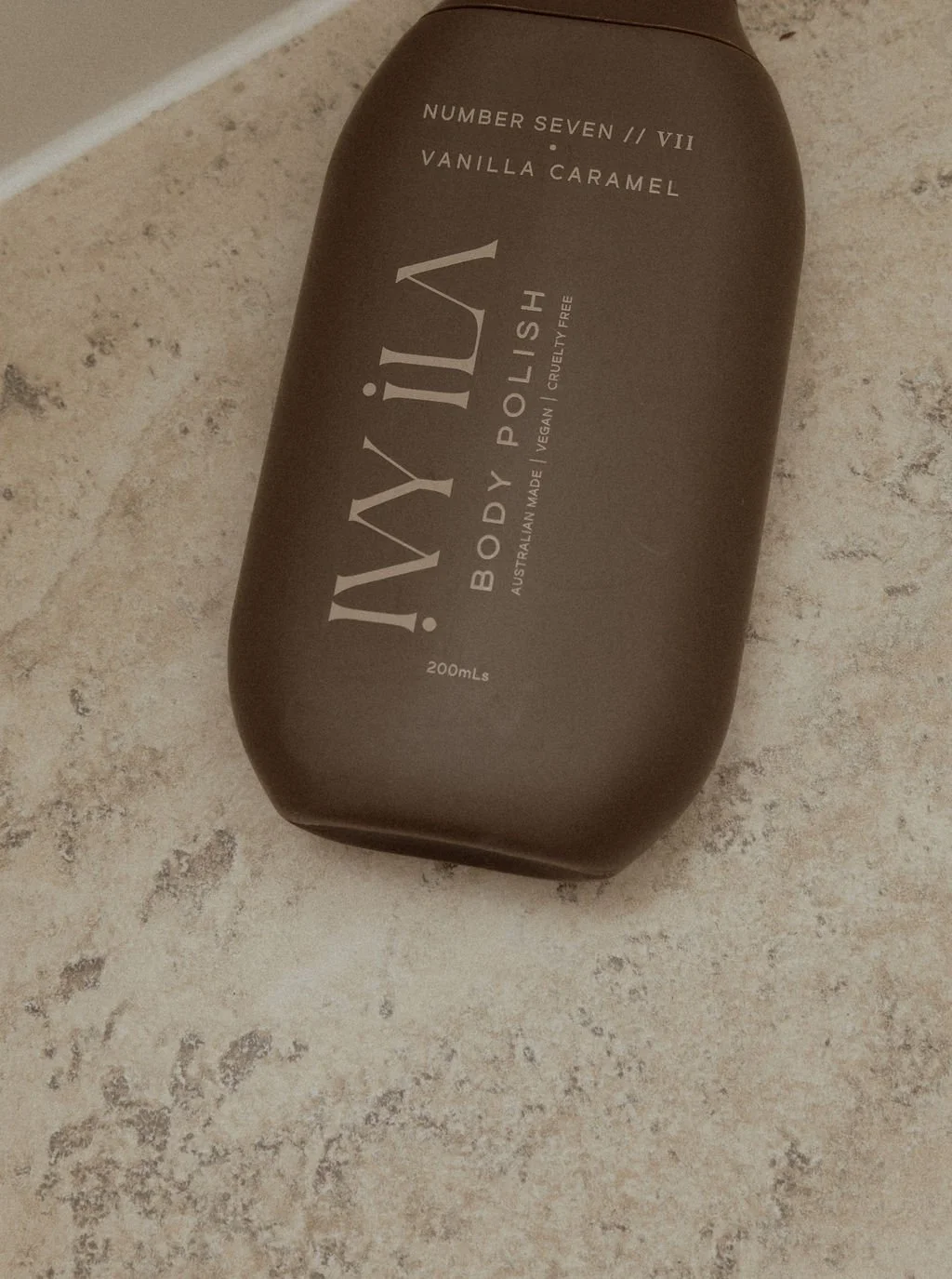 A brown bottle of body wash on a tiled surface with the label displaying vanilla caramel scent, 200ml size, cruelty free and vegan, made in Australia.