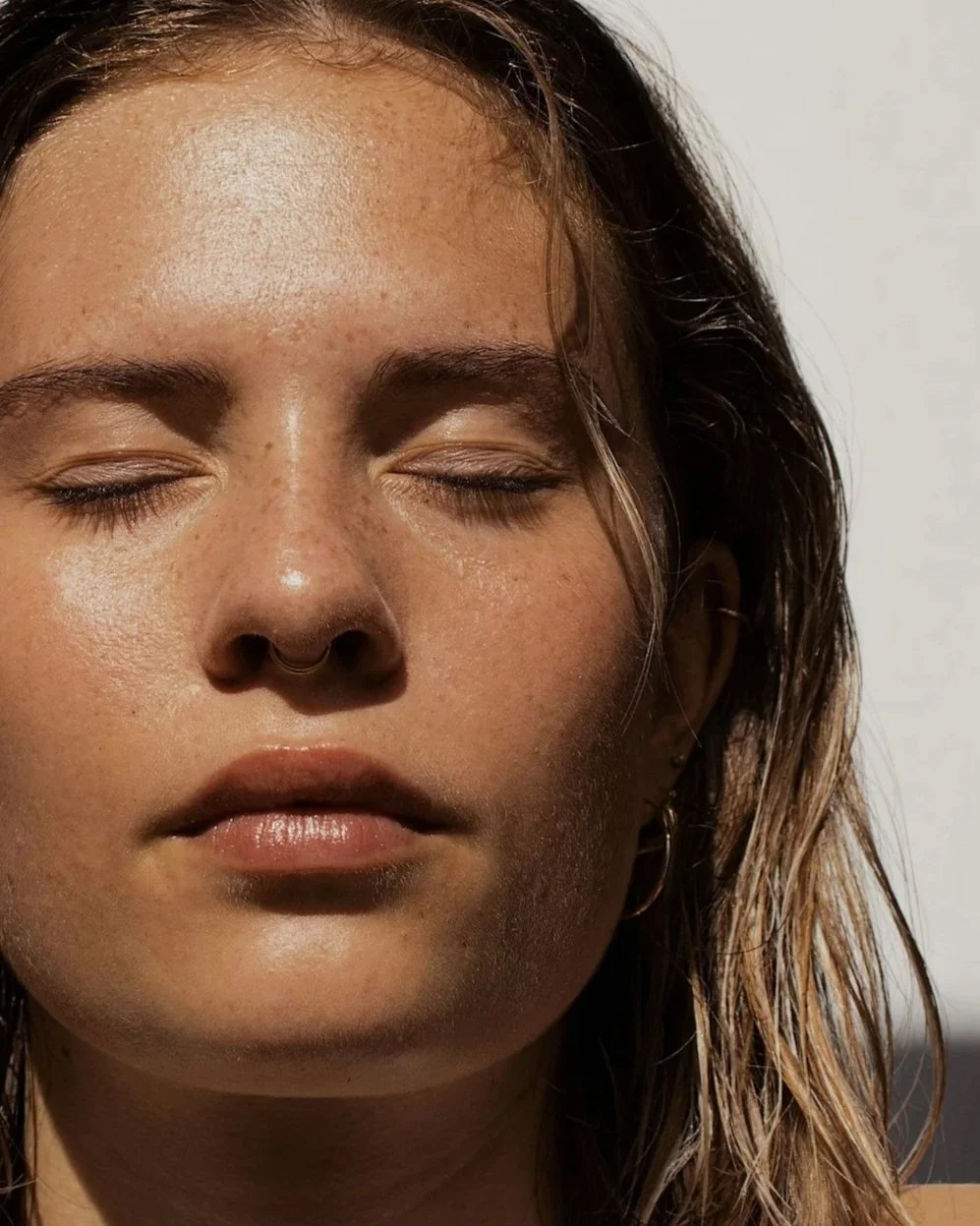 Close-up of a young woman with closed eyes, light brown skin, natural makeup, and wavy brown hair.