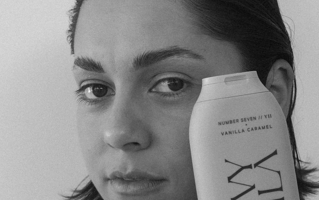 A woman with dark hair holding a white can of Vanilla Caramel ice cream close to her face.
