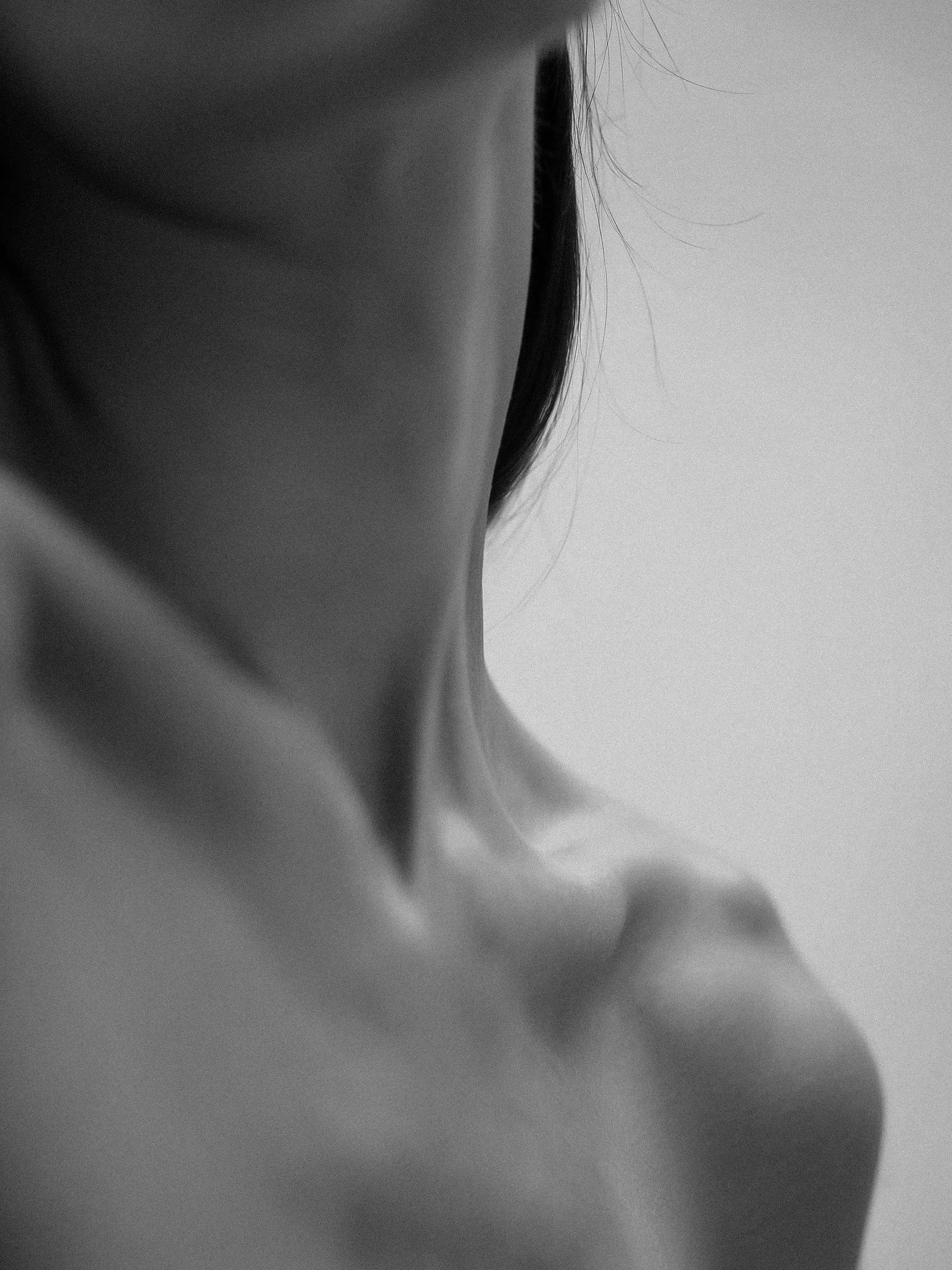 Close-up black and white photo of a person's neck, jawline, and part of their face with hair hanging loosely.