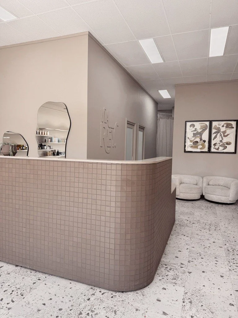 Interior of a modern room with a curved beige tiled wall, artwork on the wall, and a white curved sofa.