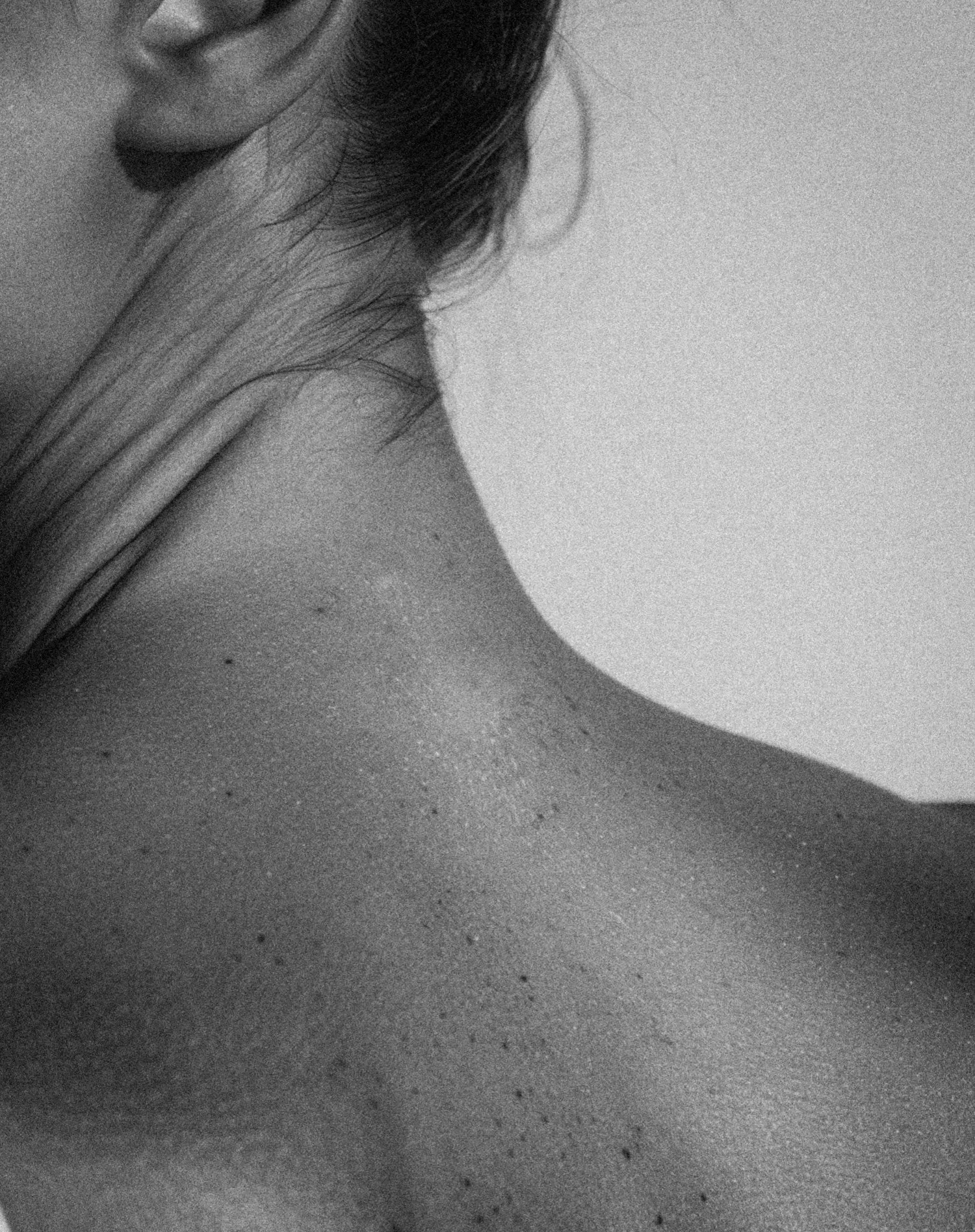 Close-up of a woman's face and shoulder in black and white, with hair partially covering her face.